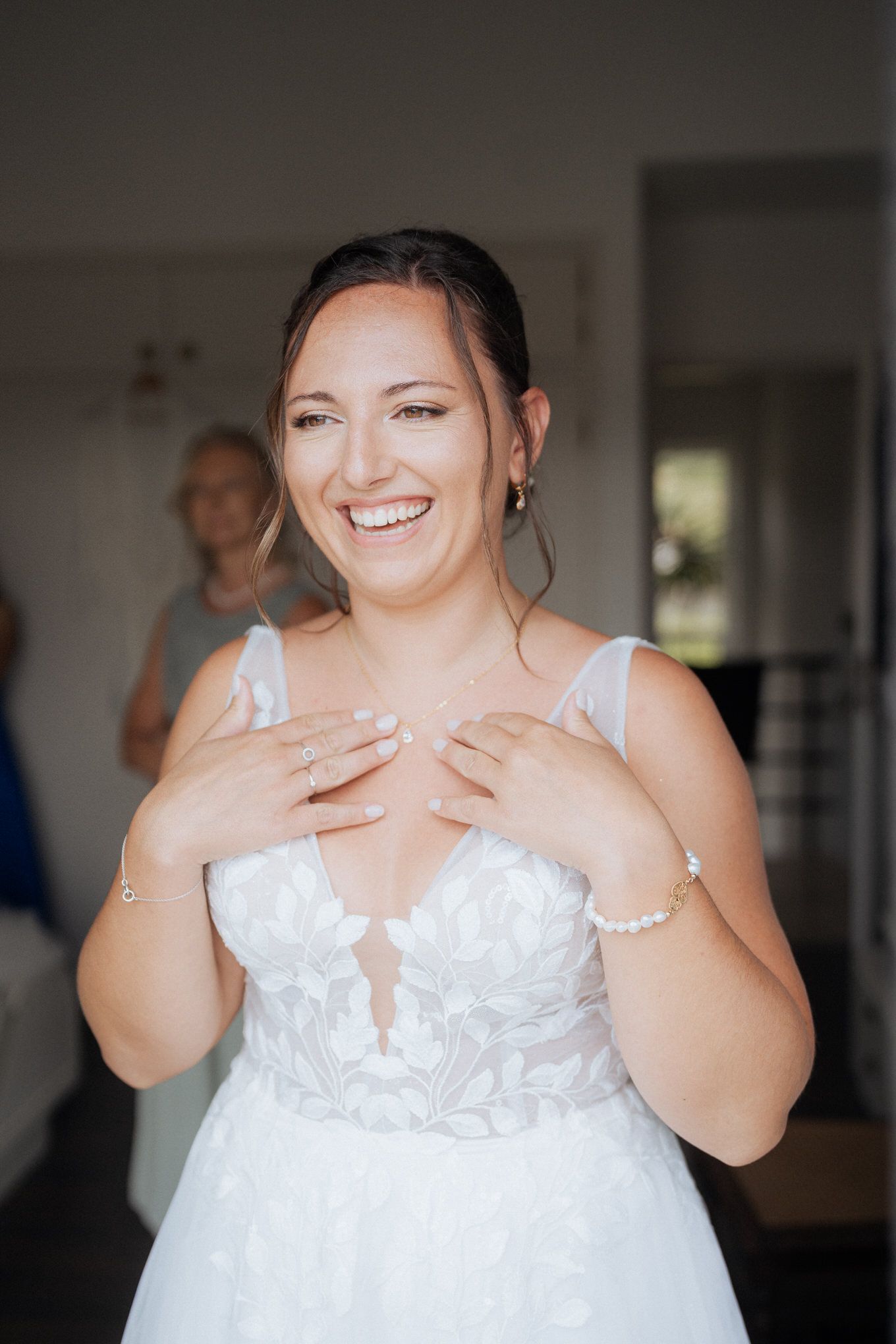 Happy bride wearing a white lace wedding dress with plunging neckline smiles while getting ready on her special day.