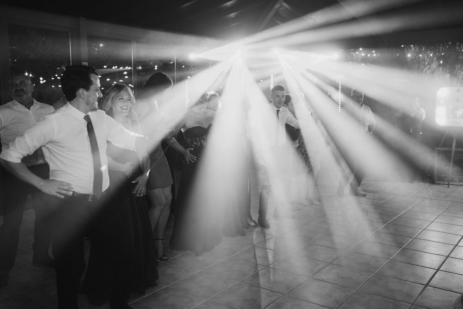 Black and white photo capturing dramatic light beams streaming across a dance floor at a wedding reception.