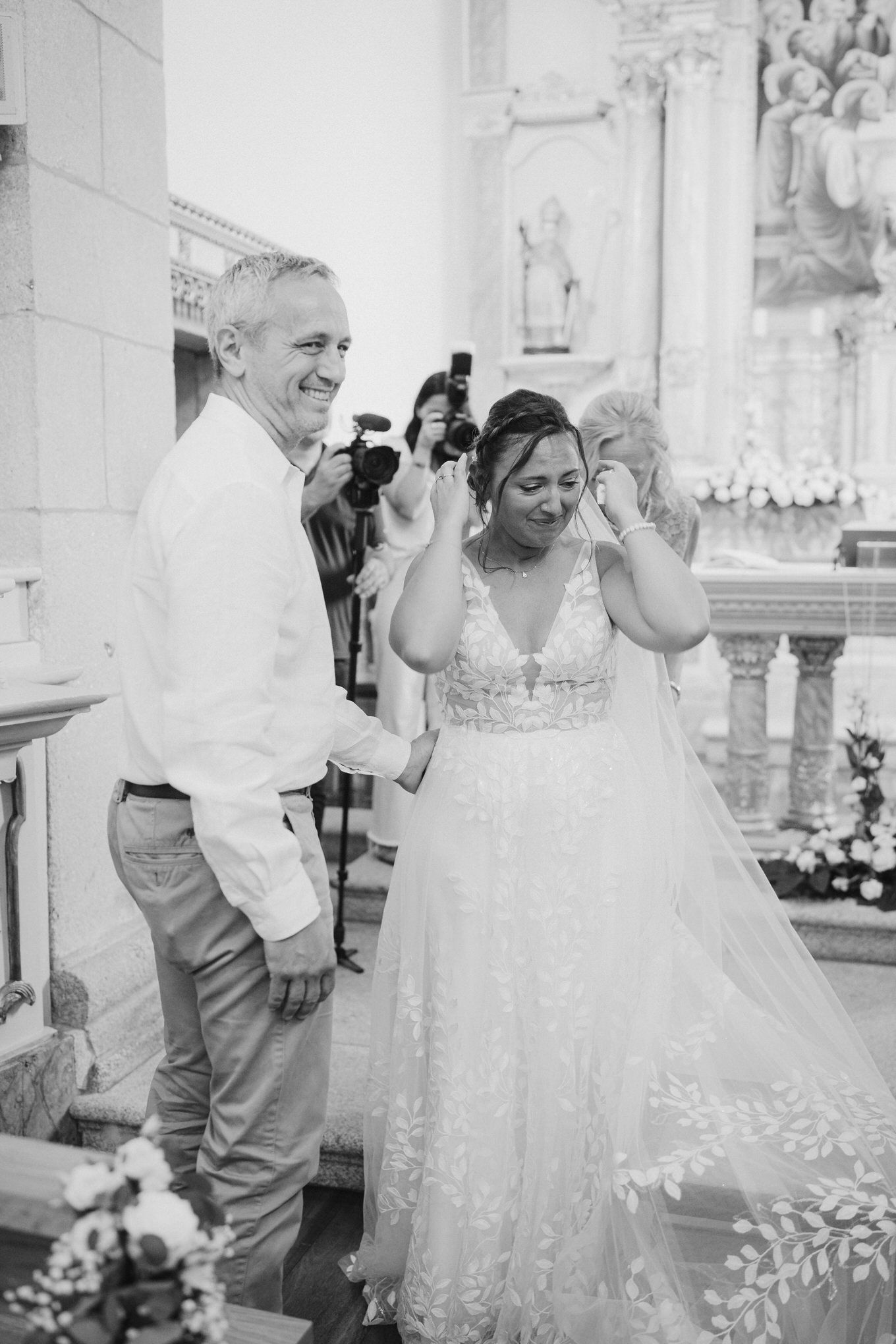 A joyful wedding moment captured in black and white at an ornate church altar with floral decorations.