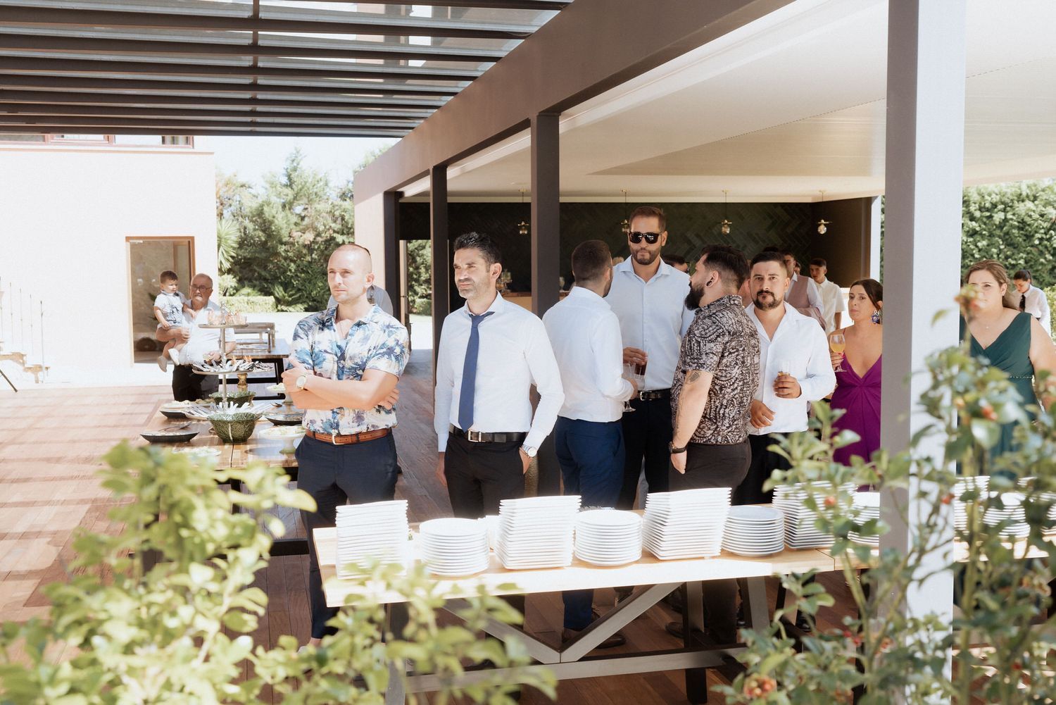 Professional business colleagues gather in an office lobby with windows and greenery visible in the background.