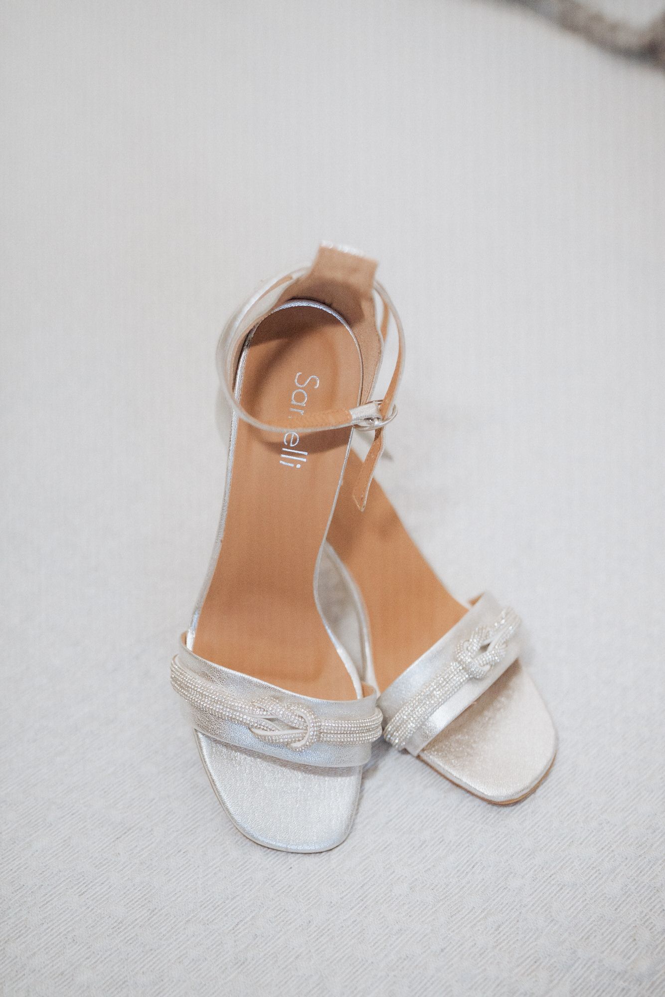 Elegant white strappy bridal sandals with ankle straps displayed on a light gray surface.