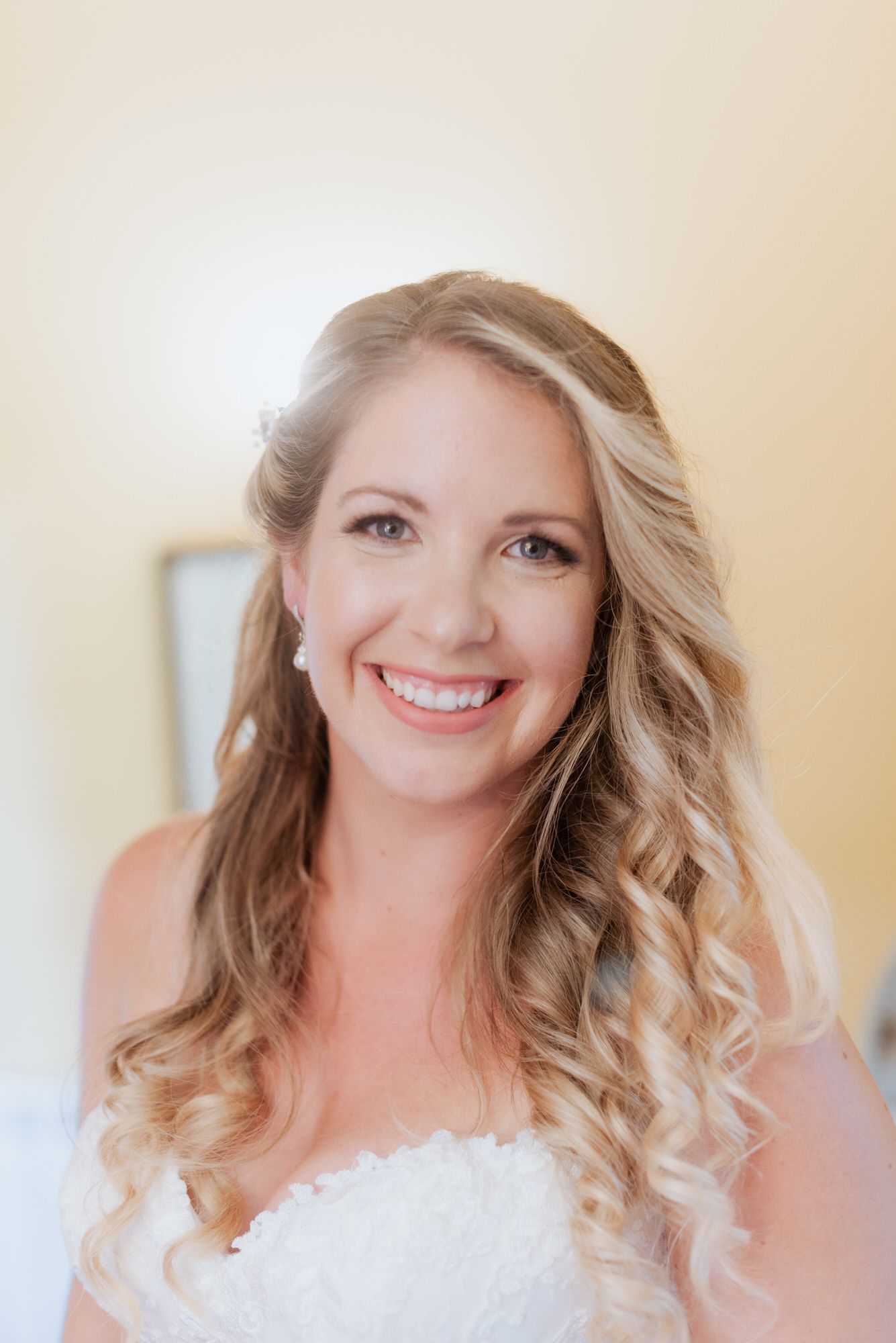 A bride on her wedding day wearing a white strapless dress with flowing blonde curled hair.