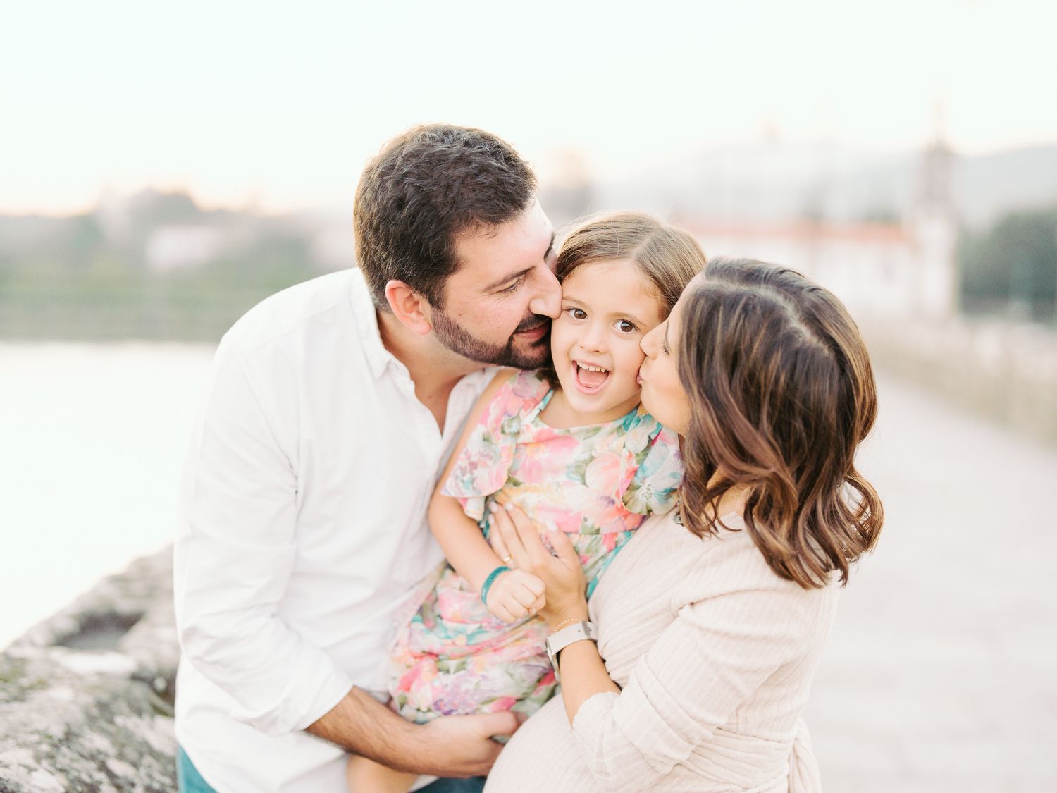 Um momento amoroso em família capturado na praia durante o pôr do sol, demonstrando afeição por seu filho pequeno em um vestido floral.