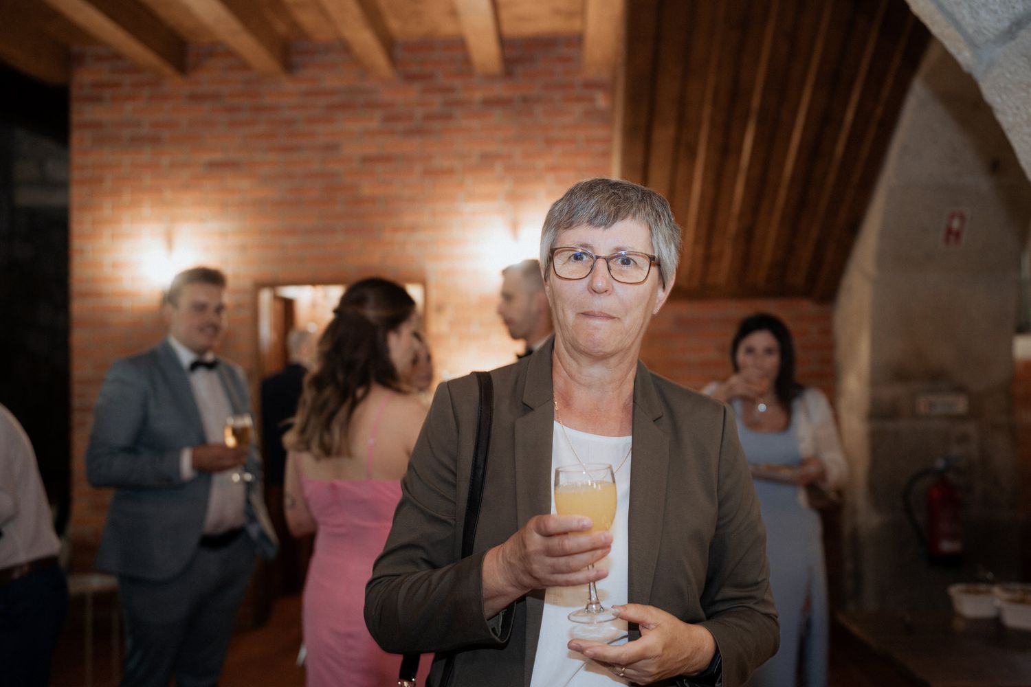 People gather at an evening event in a rustic venue with wooden beams and warm lighting.