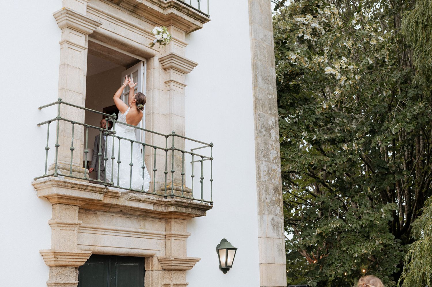 A person stands on an elegant stone balcony of a white colonial building with ornate architectural details.