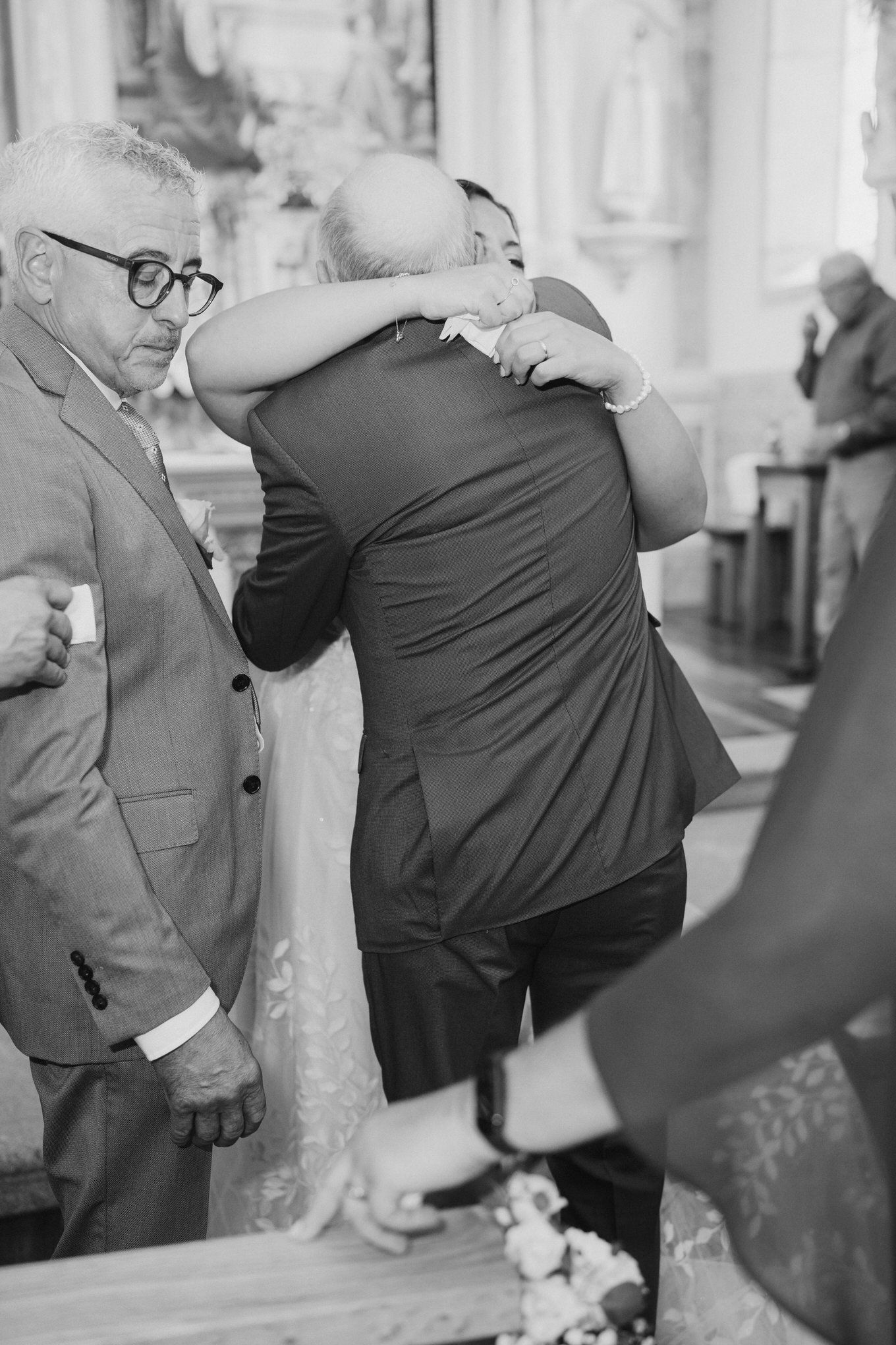 Two people share an emotional embrace at what appears to be a formal event, captured in black and white photography.