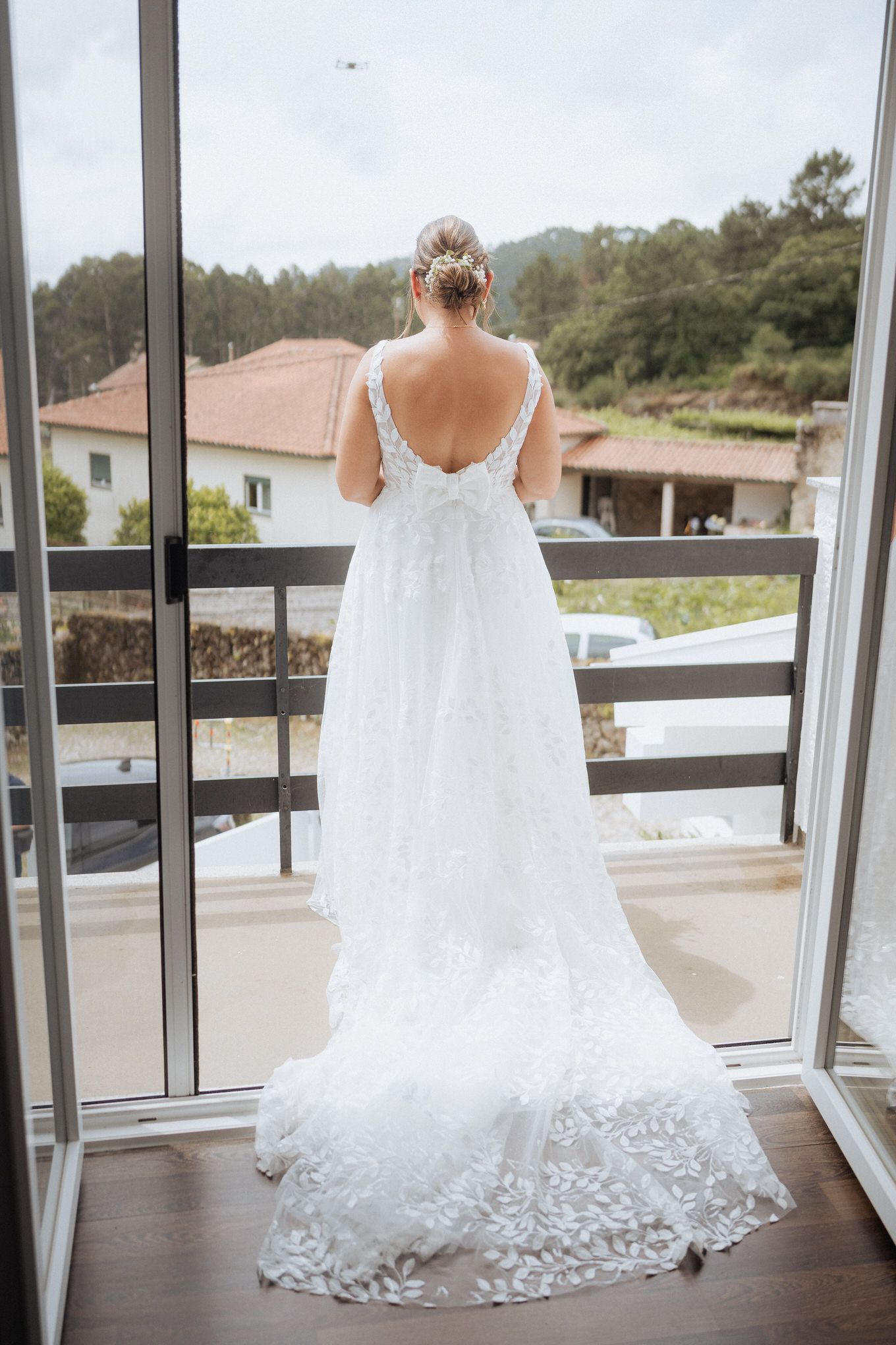 Back view of a bride in an elegant white lace wedding gown with long train standing on a balcony.