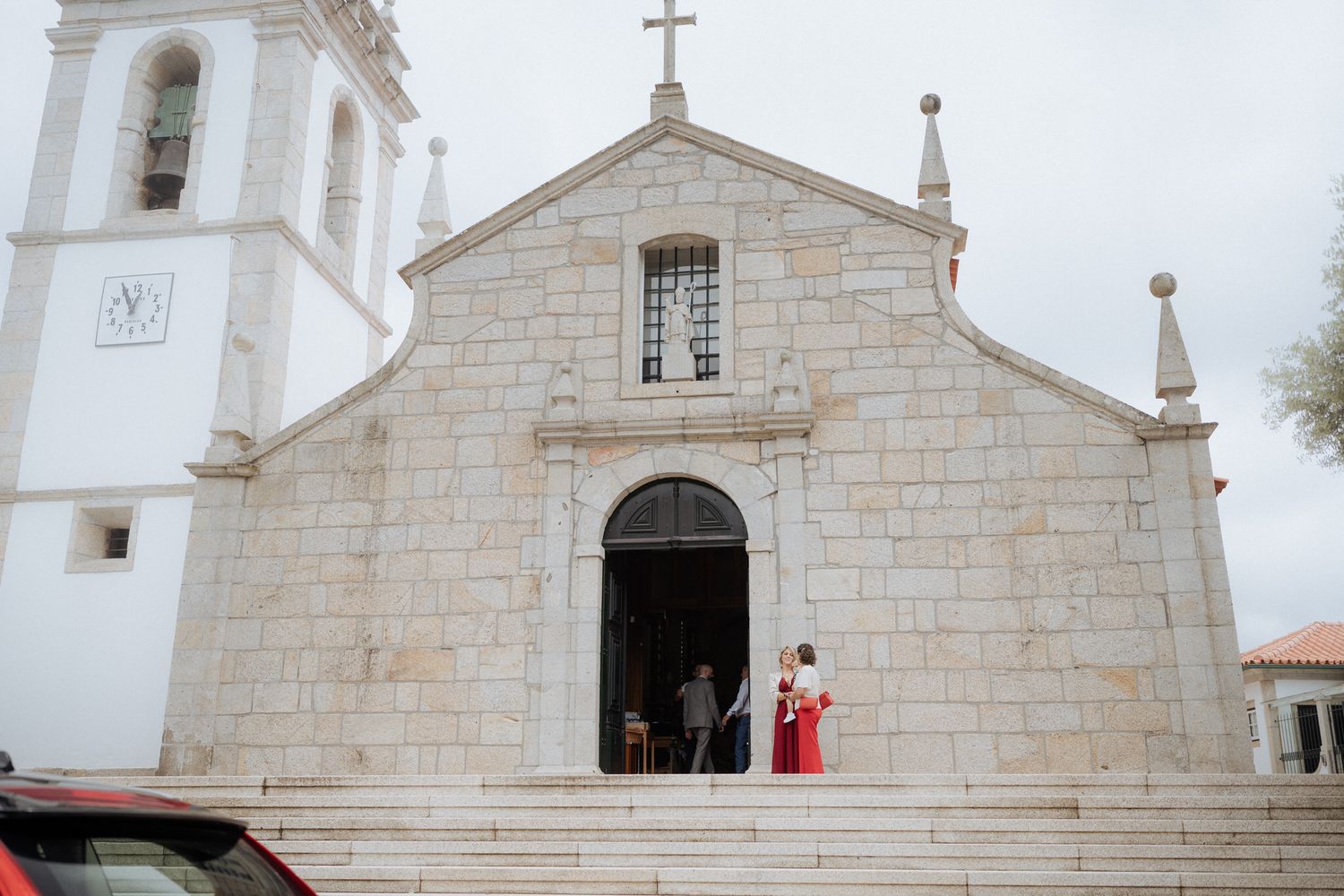 Traditional white stone Portuguese catholic church with arched entrance and bell tower against bright sky.