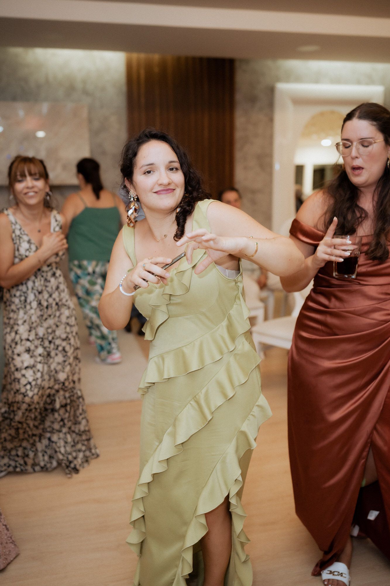 People dancing and having fun at a wedding reception on a wooden dance floor, with one person wearing a mint green dress.