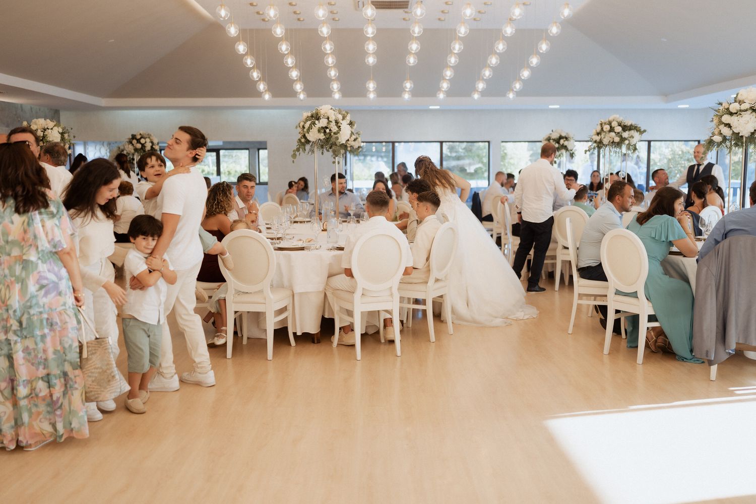 Panoramic view of an elegant wedding reception venue with white tables and sparkling string lights overhead.