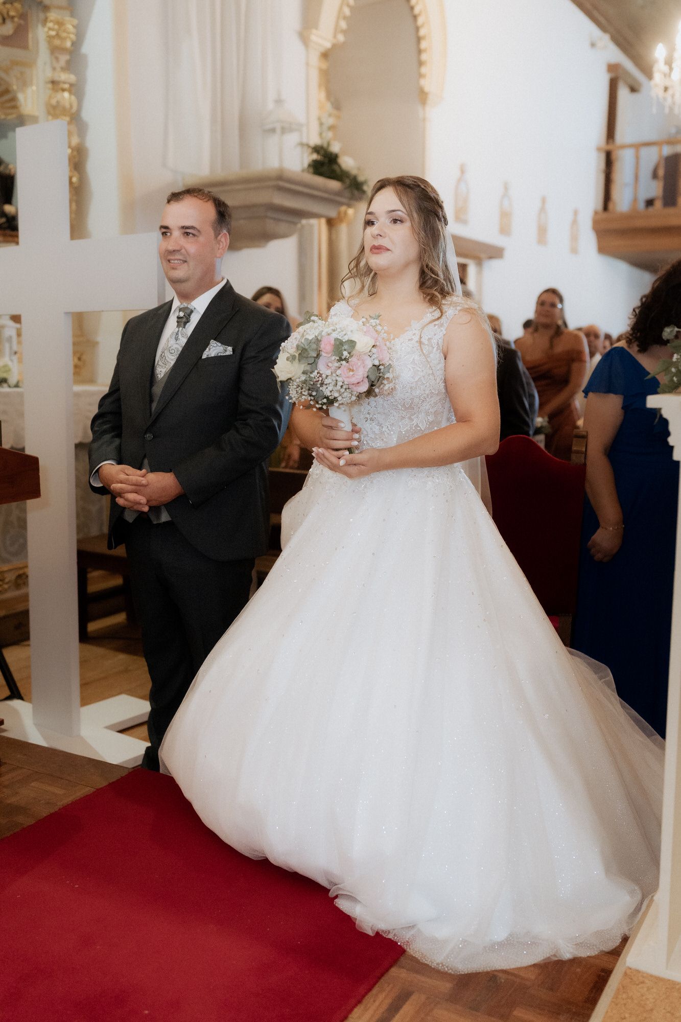 A wedding ceremony in a church with a couple standing at the altar on a red carpet.