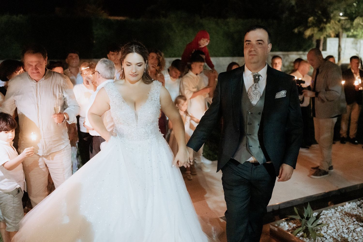 A couple dances together at their evening wedding reception surrounded by guests with sparklers.