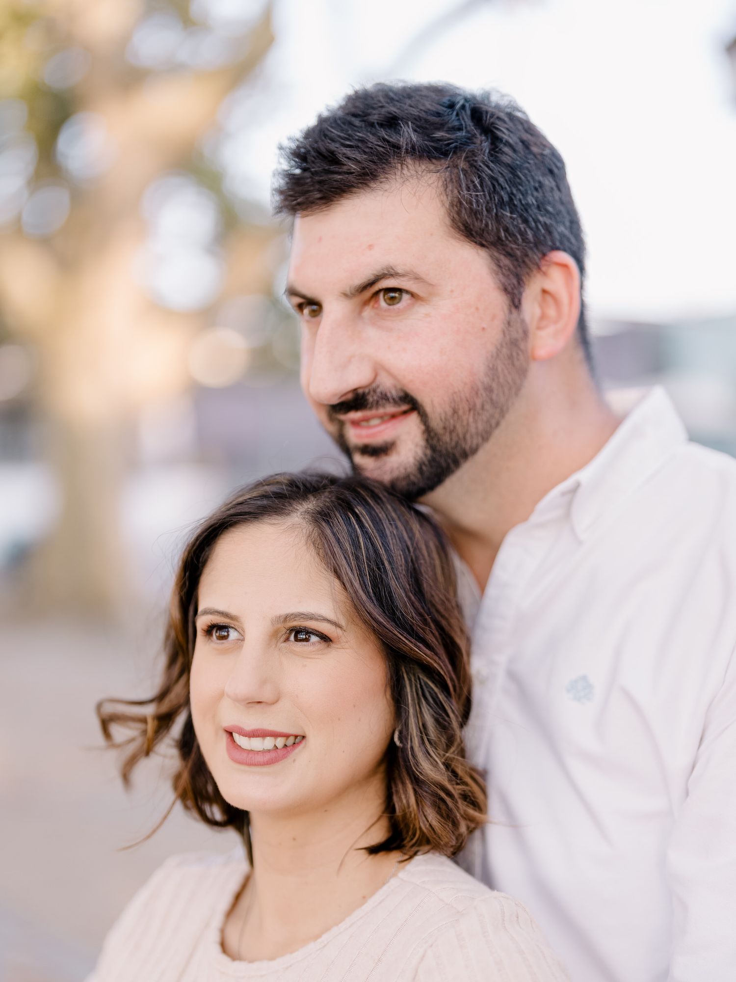 Um casal posa intimamente para um retrato ao ar livre com iluminação suave e roupas de cores neutras.