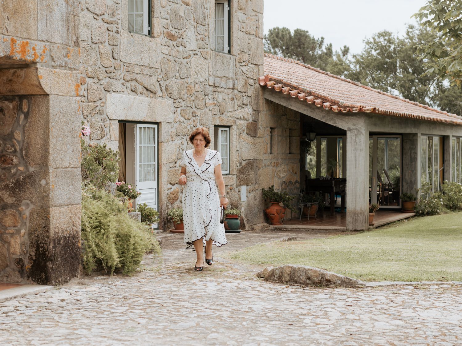 White linen dress against rustic stone walls and terracotta tile roof of vintage countryside estate.