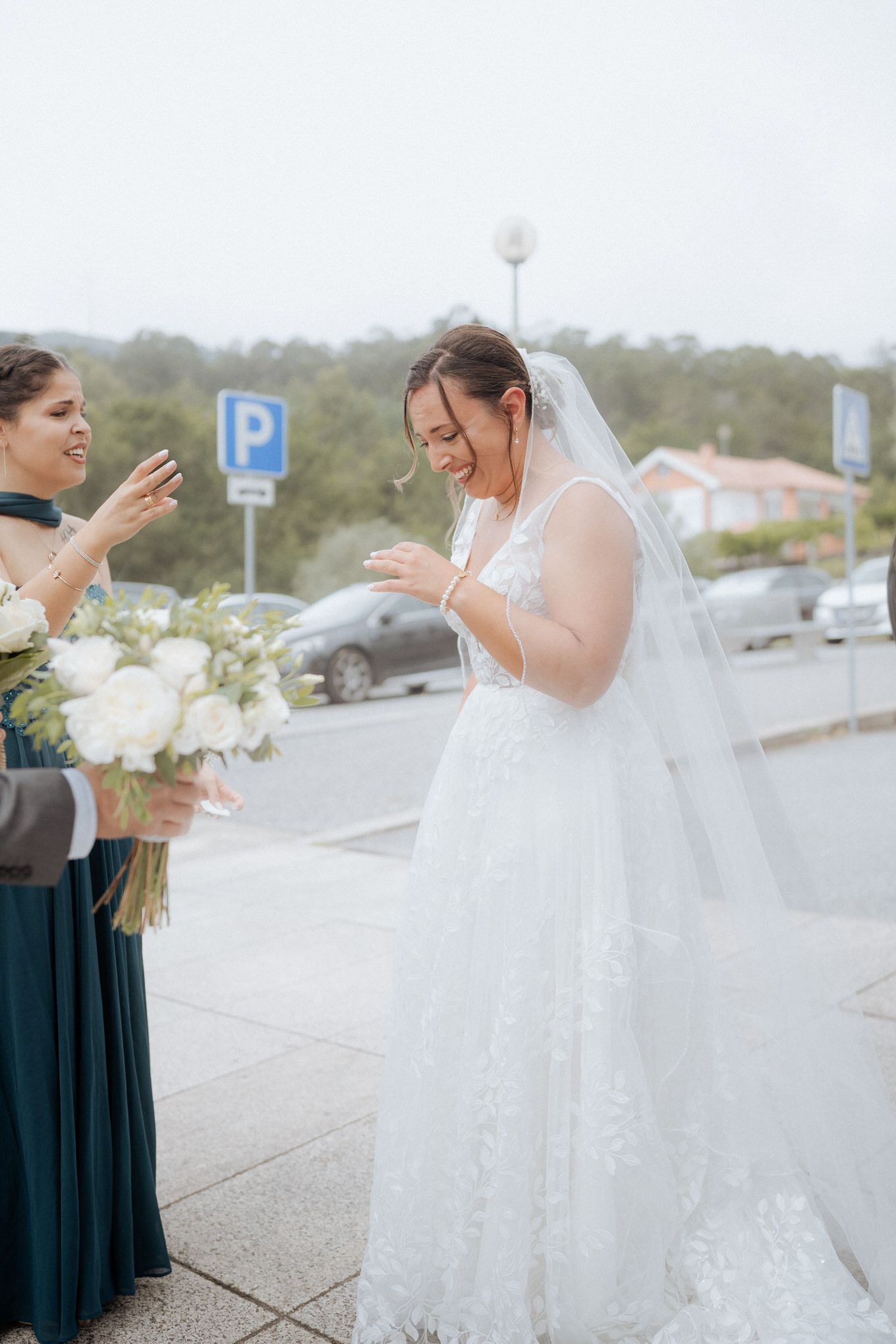 A joyful moment captured between a bride in white and bridesmaid in teal sharing laughter outside.