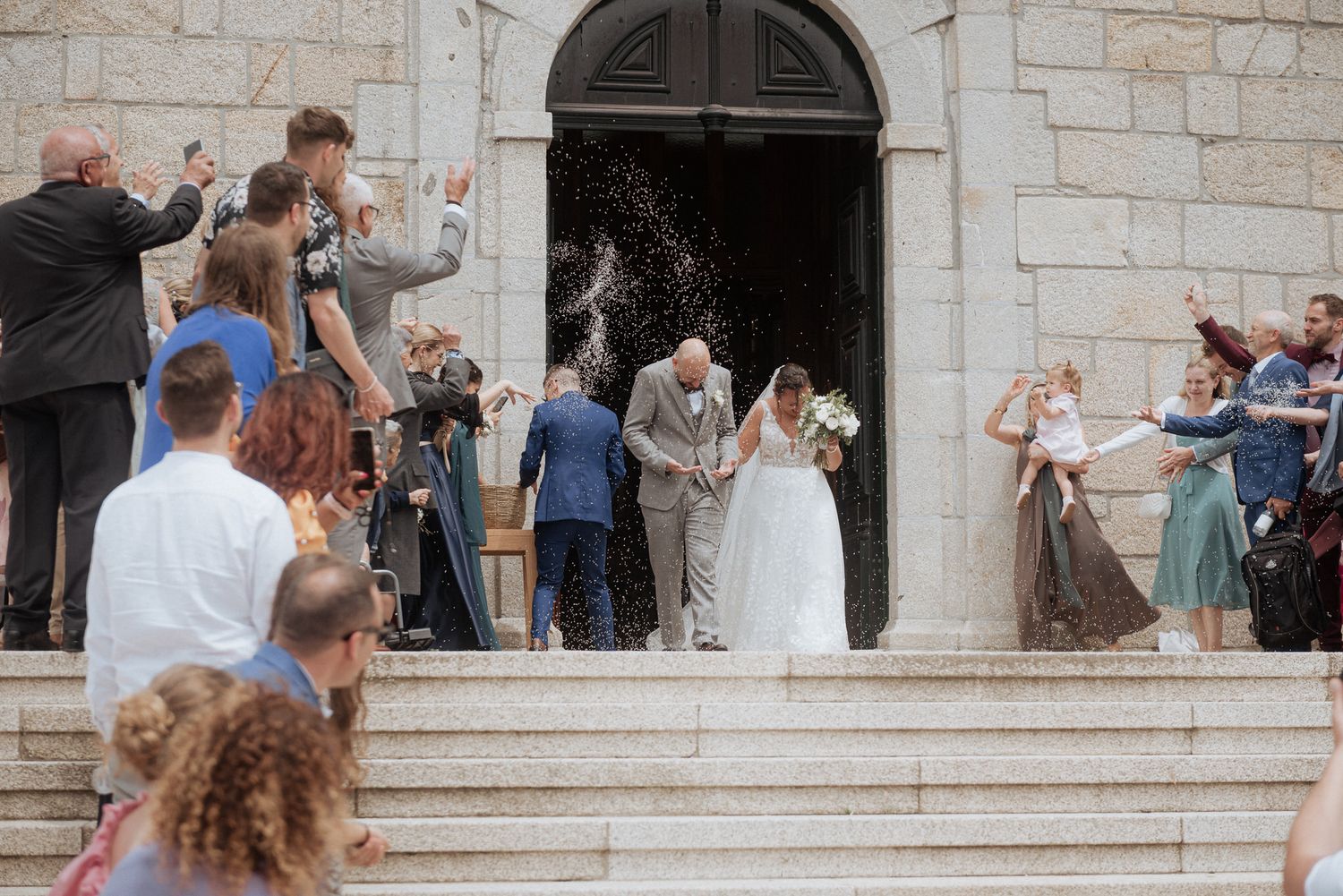 Wedding guests throw rice as newlyweds exit stone church steps on their special day.