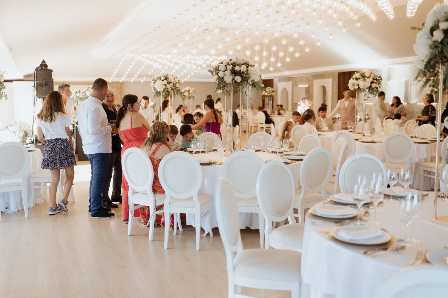 Elegant wedding reception venue with white chairs and tables decorated with floral centerpieces under glowing lights.