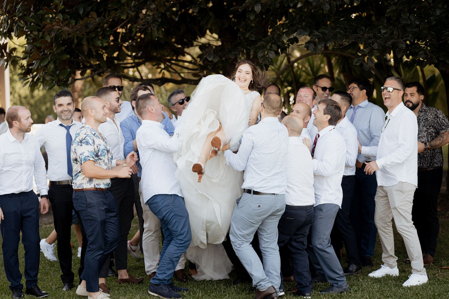A joyful wedding celebration scene with a group of people wearing white and blue attire gathered outdoors.