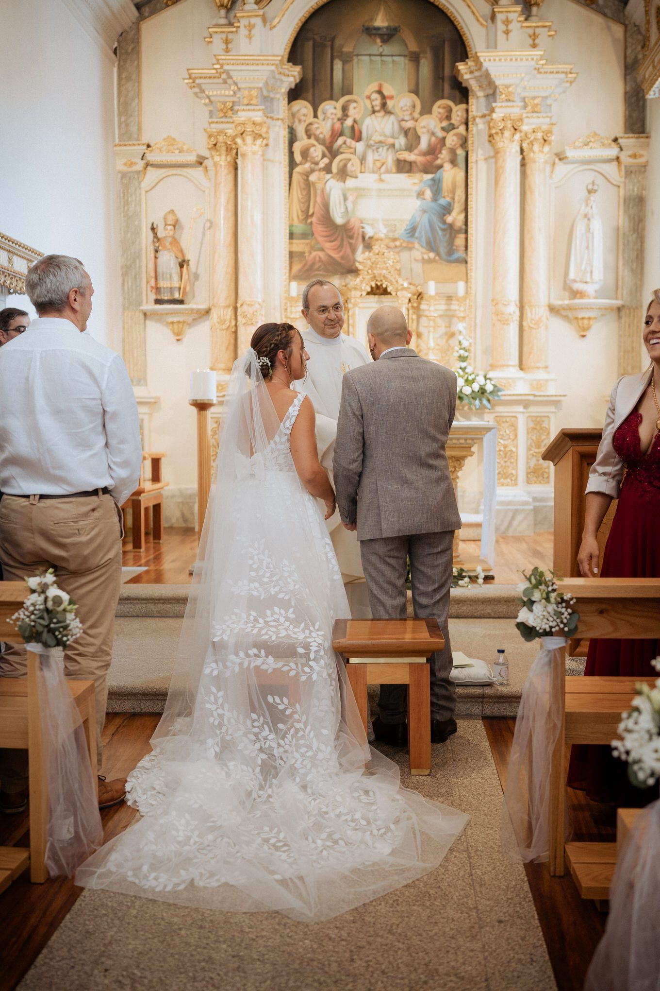A Catholic church wedding ceremony with an ornate altar and a bride in a flowing lace gown with long train.