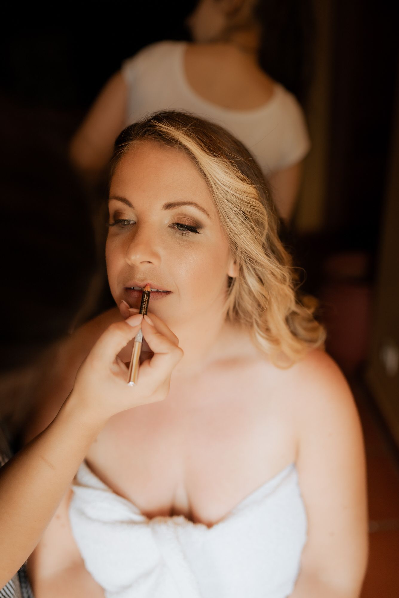 A cinematic image capturing a bride getting her makeup done with warm lighting in an intimate getting-ready moment.