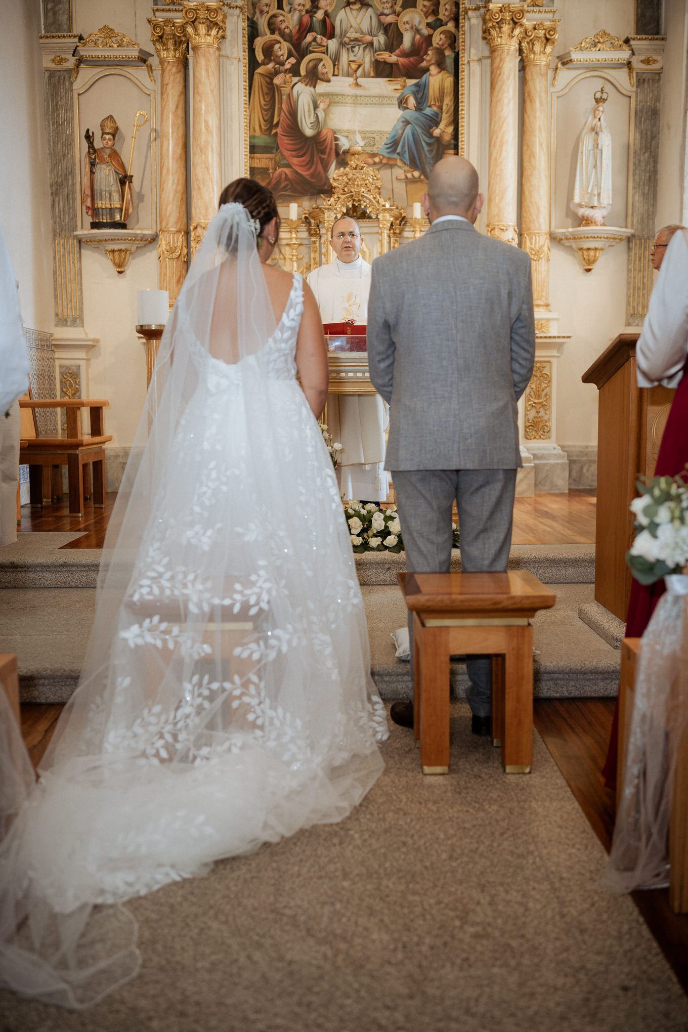 A couple stands at the altar of an ornate Catholic church during their wedding ceremony.