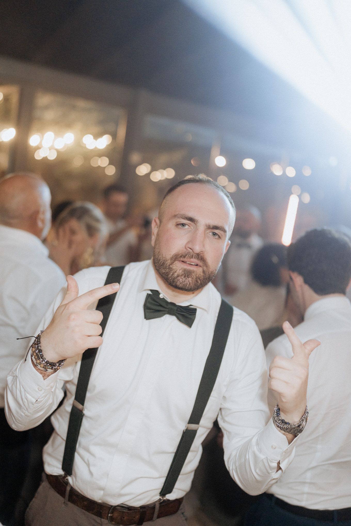 A guest at a formal event gives thumbs up while wearing a white dress shirt, black bow tie and suspenders.