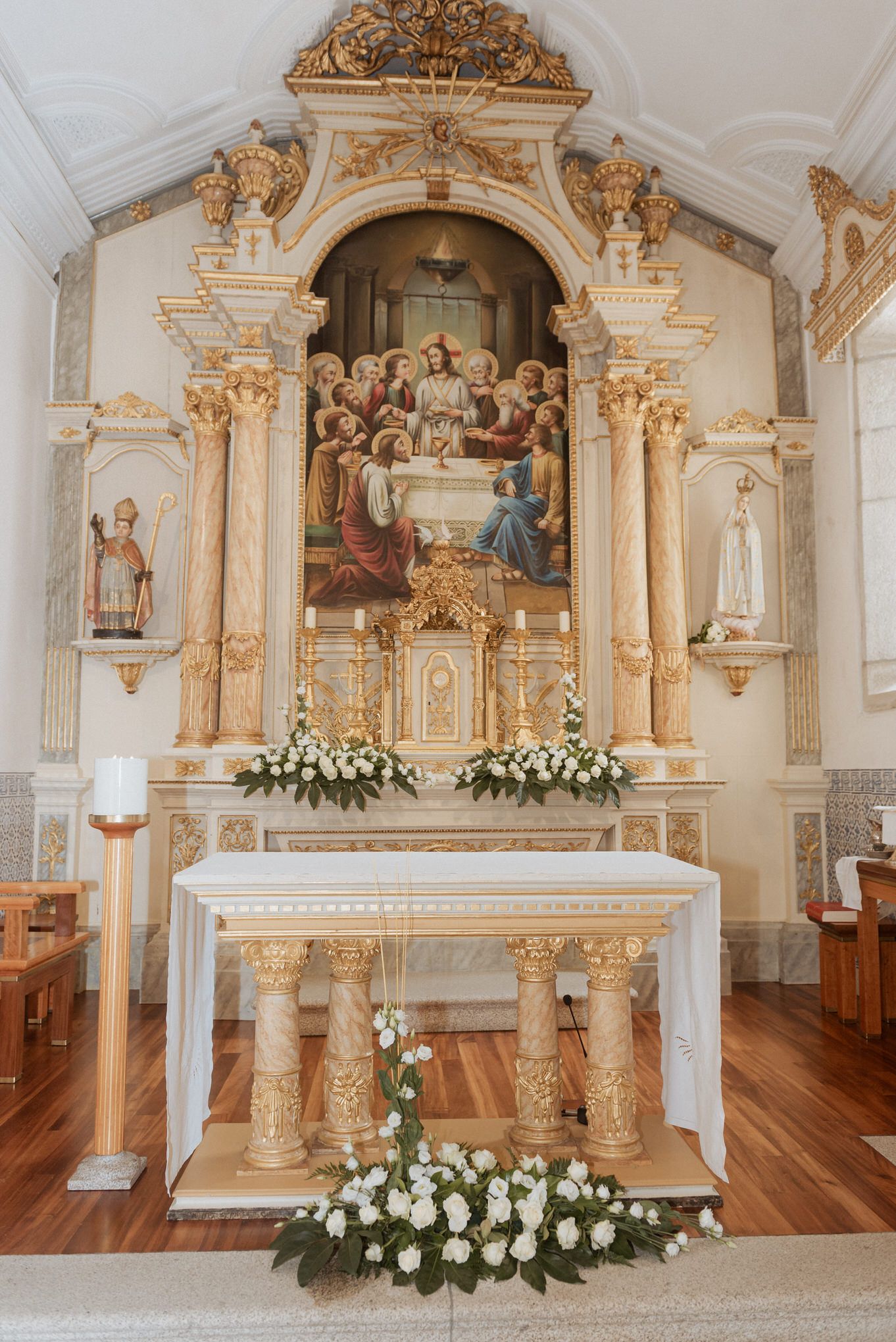 Ornate baroque church altar with gilded columns and religious artwork, decorated with white floral arrangements.