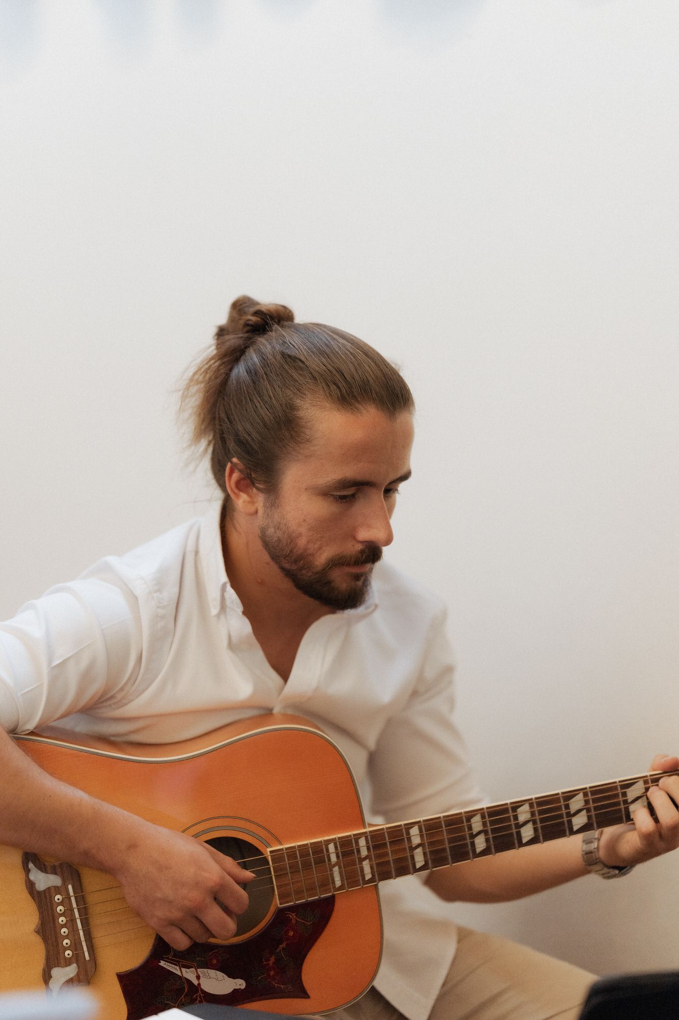 A person in a white shirt plays an acoustic guitar while seated in three progressive action shots.