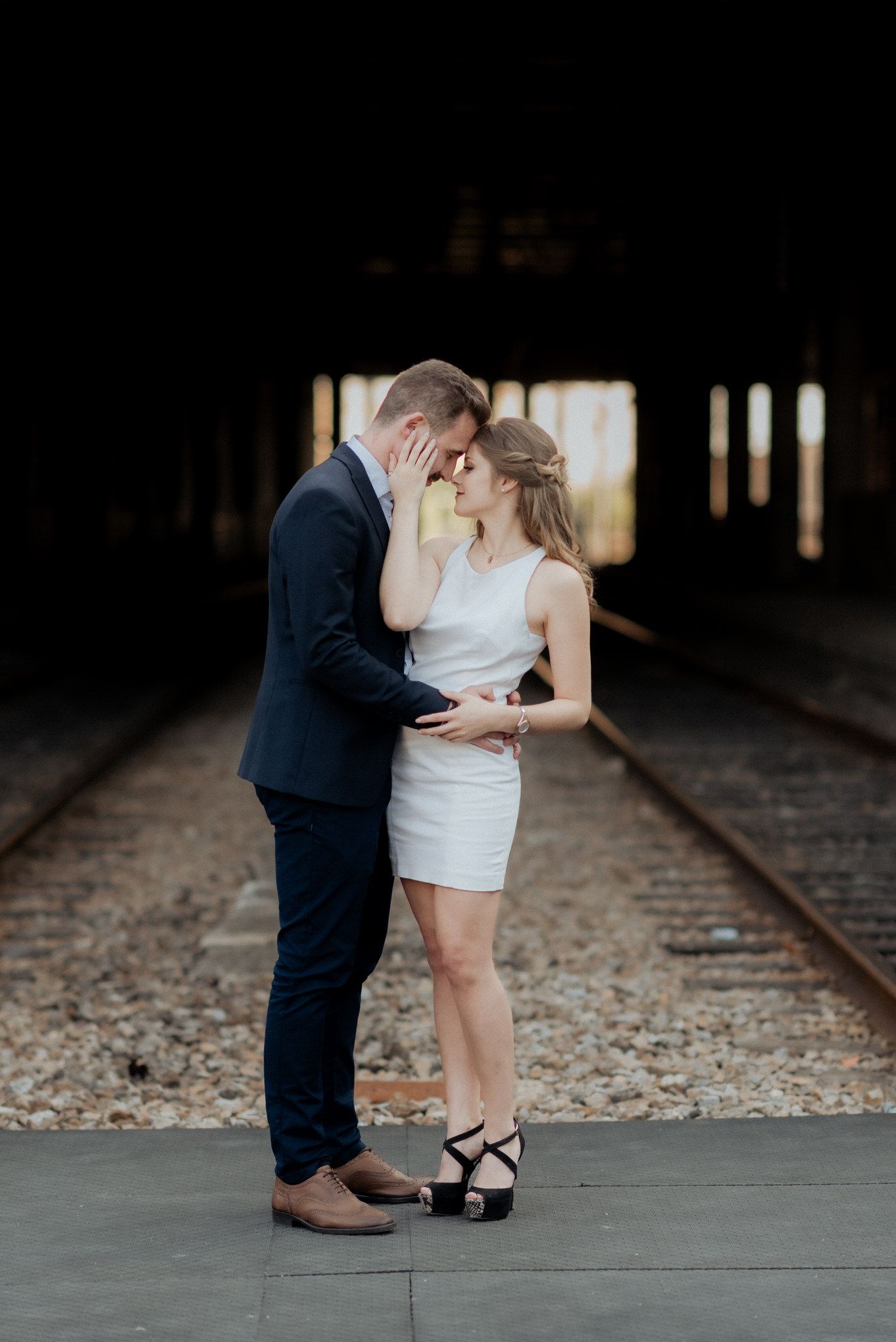 Um casal romântico compartilha um momento íntimo nos trilhos do trem com pouca luz.
