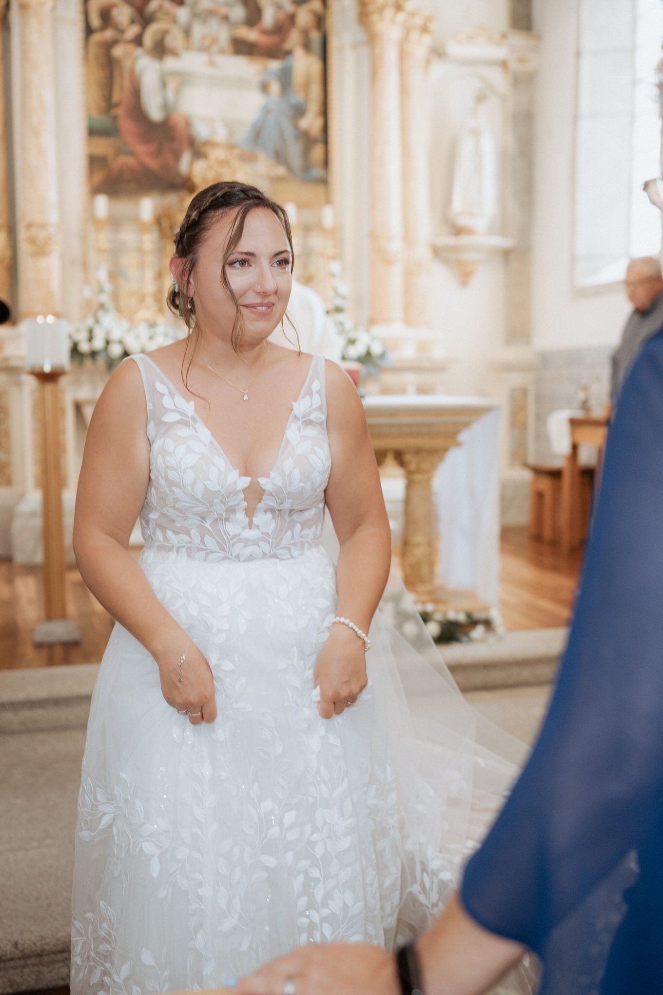 A bride wearing an elegant white lace wedding dress smiles while standing in a beautiful church setting.