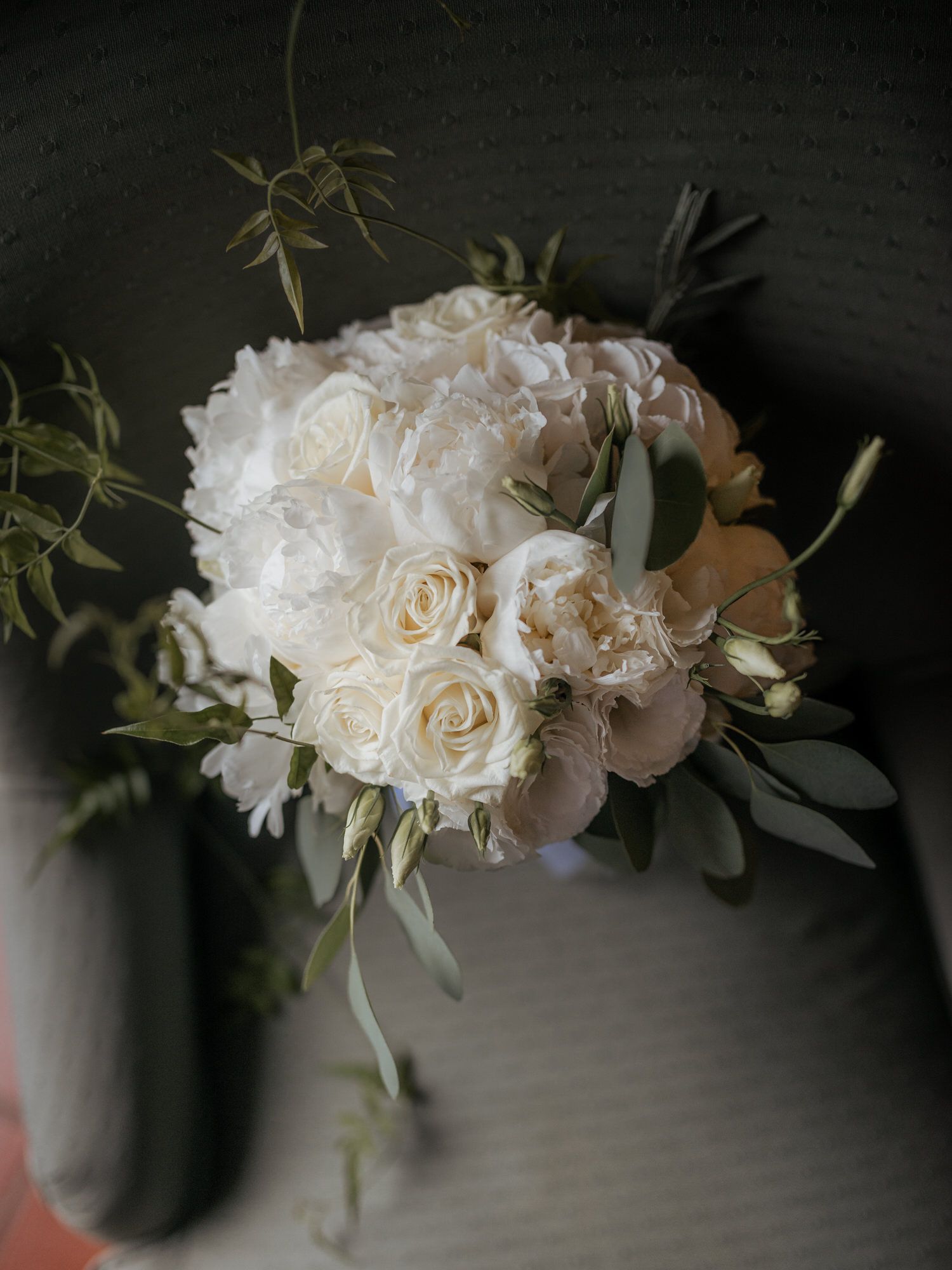 An elegant white bridal bouquet featuring roses and greenery arranged against a dark background.