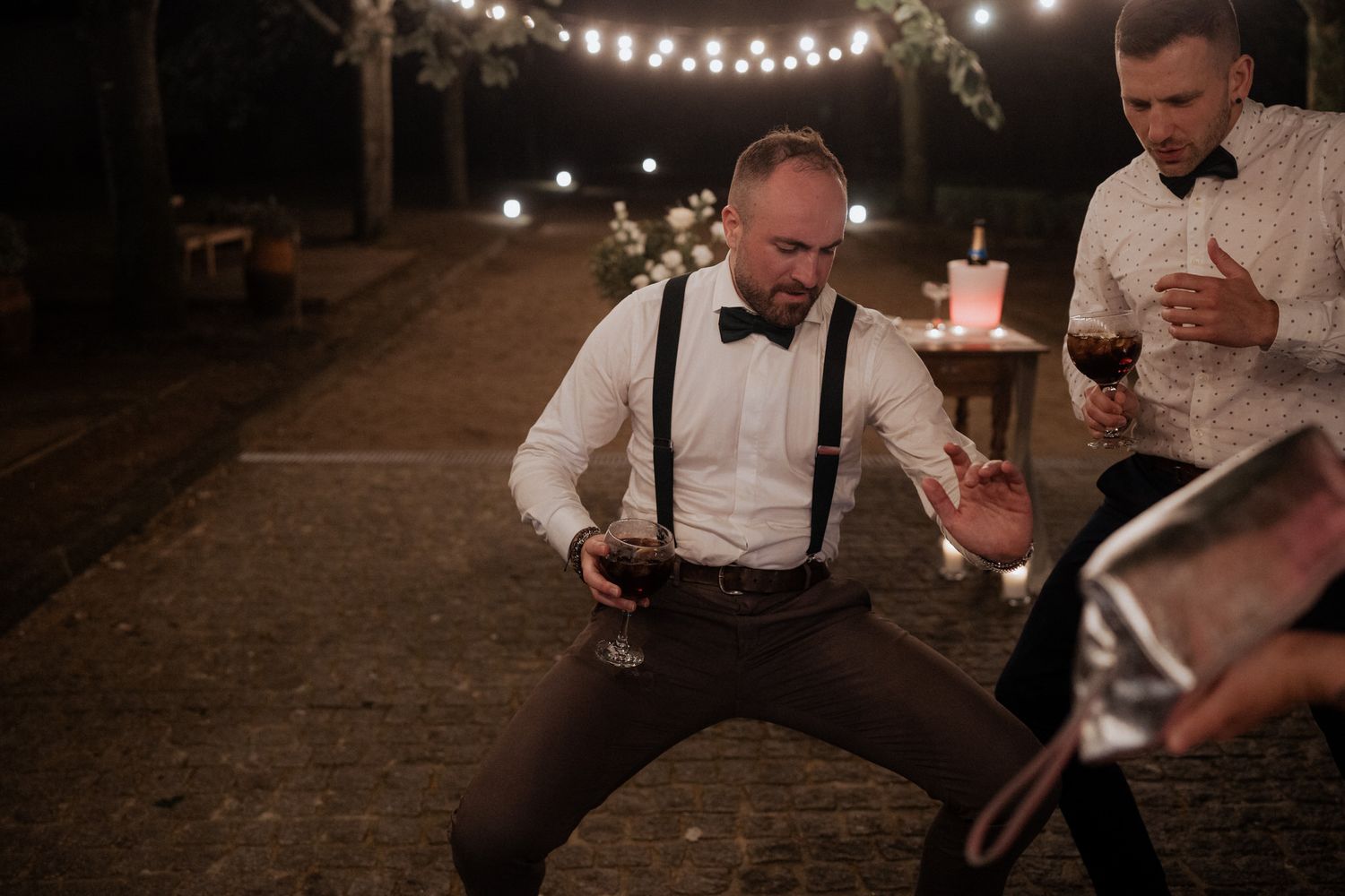 Wedding guest dancing energetically under outdoor string lights at a nighttime reception celebration.