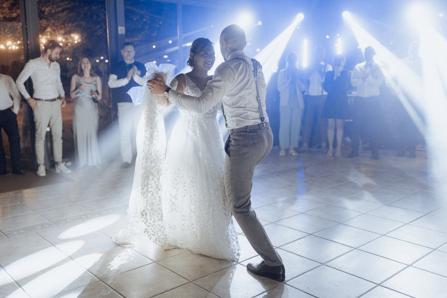 Couple performs their first dance at a wedding reception with smoke and dramatic lighting on a white tile dance floor.