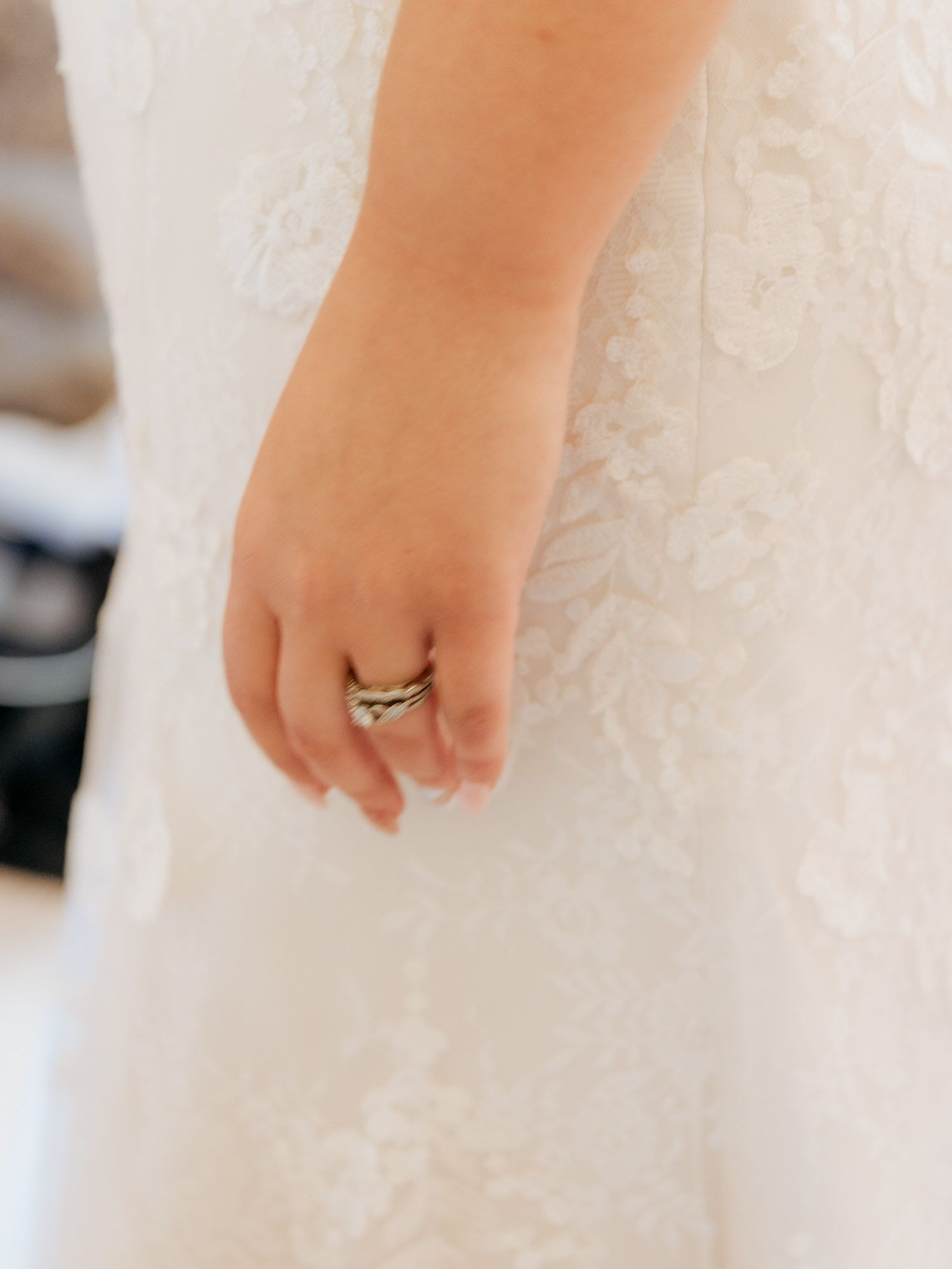 Close-up of a delicate hand wearing an elegant chevron-style wedding ring against a white dress background.