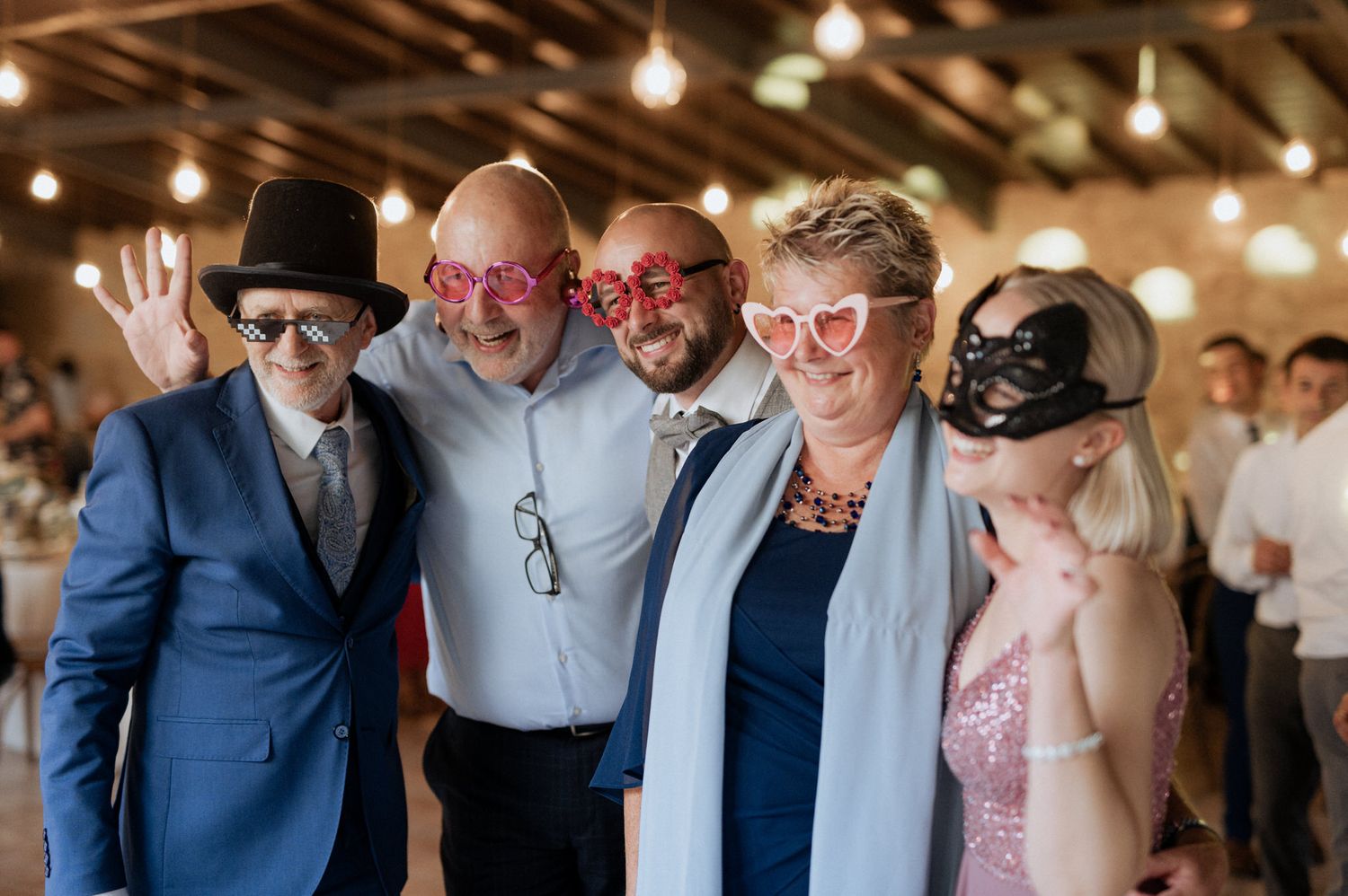 Group of party guests wearing colorful novelty eyewear and masks posing together at an indoor celebration.