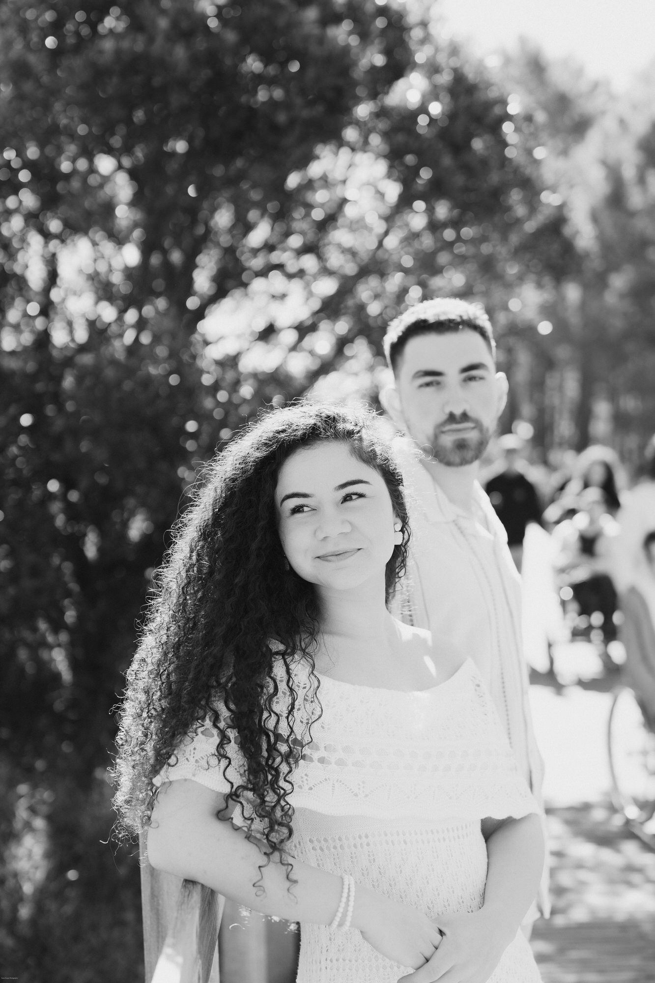 Foto em preto e branco de um casal ao ar livre com linda iluminação bokeh. A mulher tem cabelos longos e cacheados.