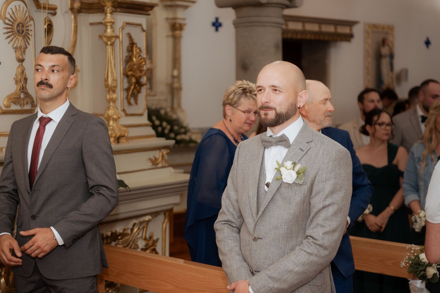 Wedding attendees gathered in ornate church pews with baroque altar decorations visible in the background.