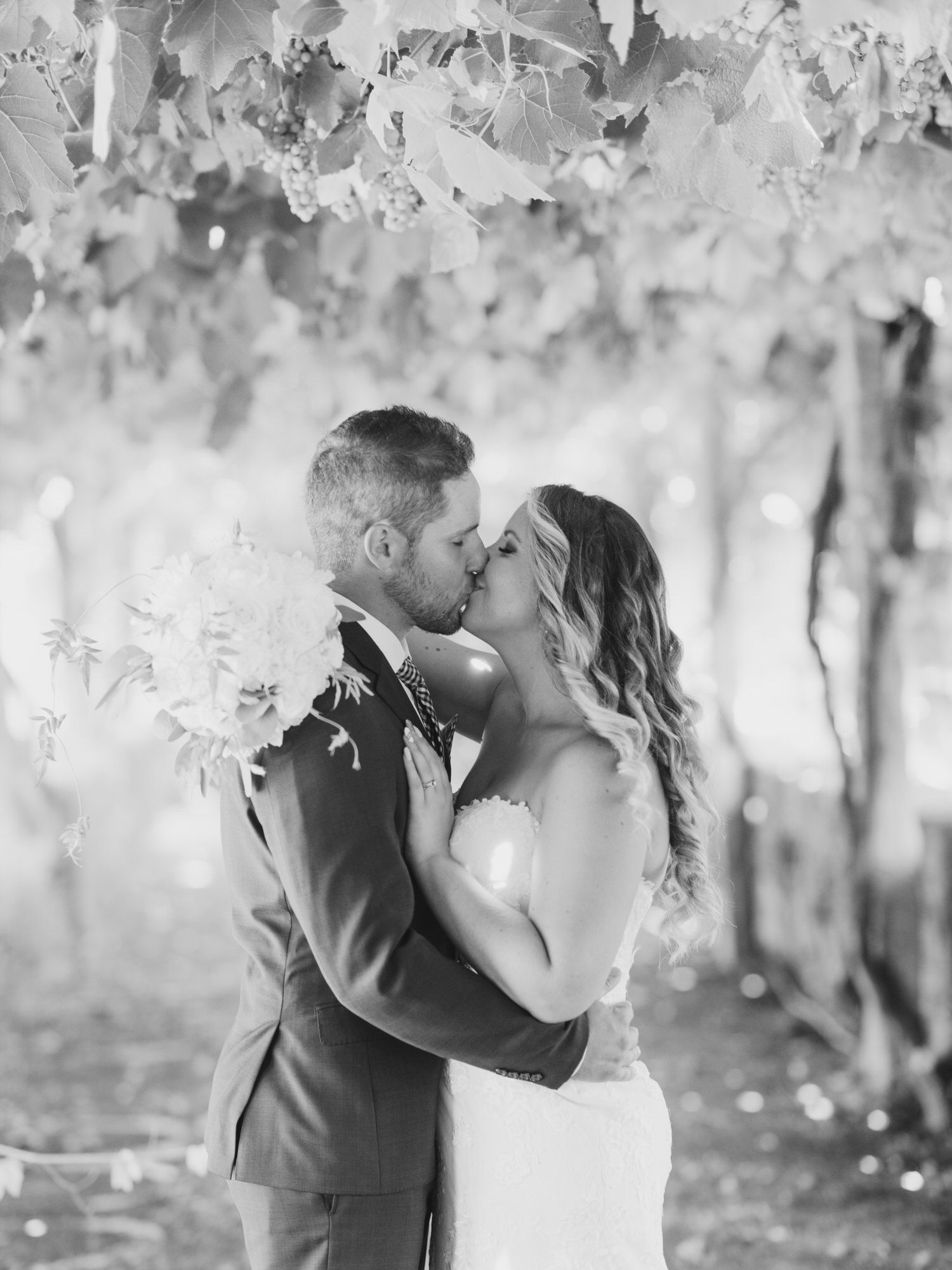 Romantic black and white wedding photos show couple sharing kisses under hanging white floral decorations.