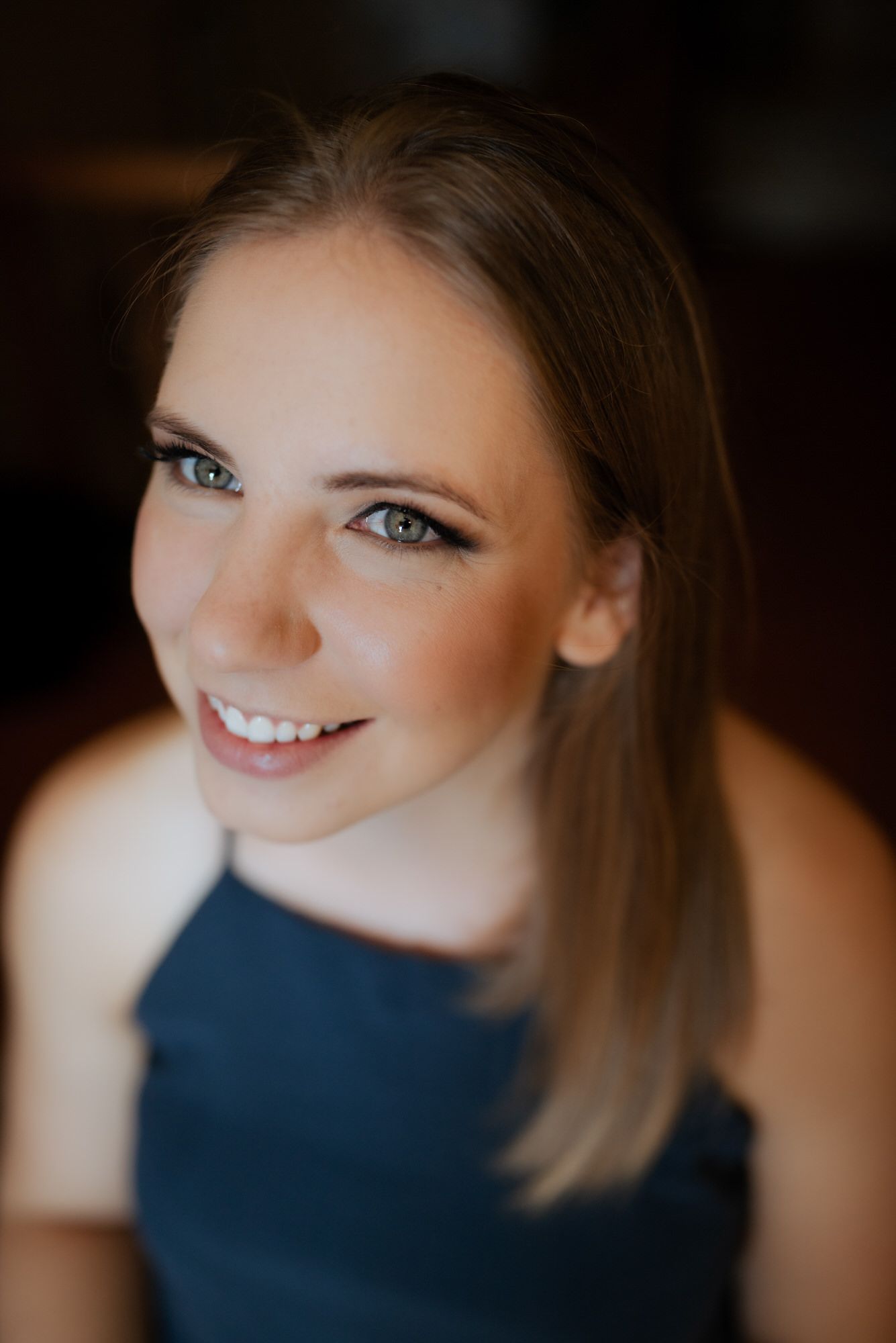 Close-up portrait series of someone with bright eyes and warm smile wearing a navy blue top against dark background.