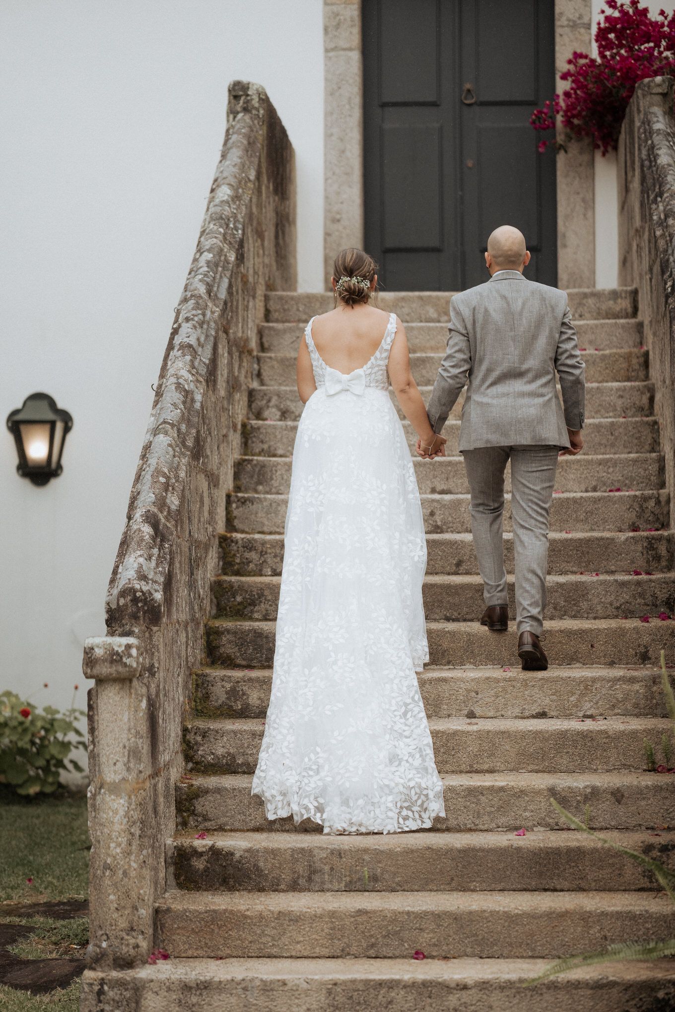 A bride and groom in formal attire climb stone steps together outside a historic building.