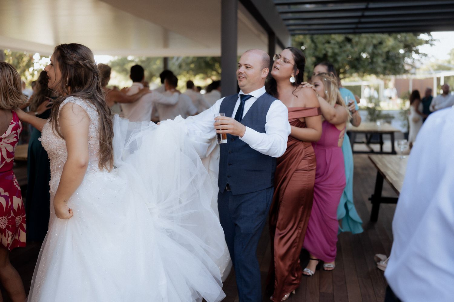 Wedding guests and a bride gather under a covered outdoor area during a celebration event.