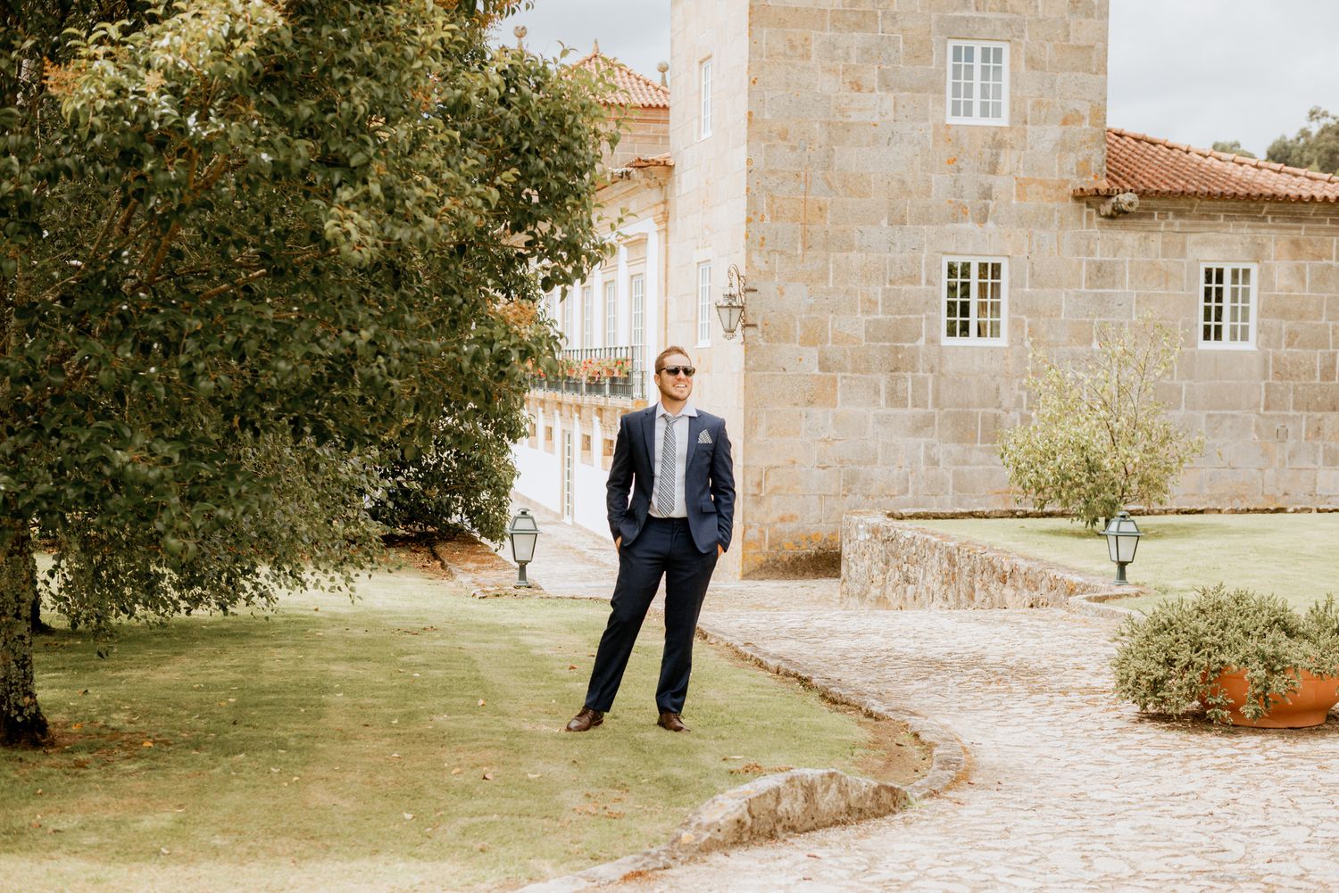 Two people walking together on a stone path outside a rustic Mediterranean villa in warm afternoon light.