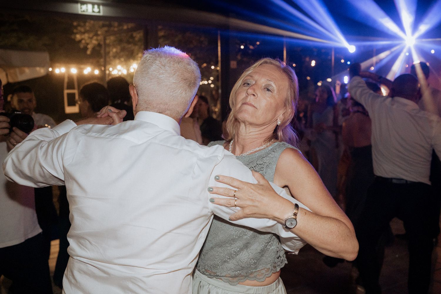 Two people slow dancing together at a nighttime event with blue lighting effects in the background.