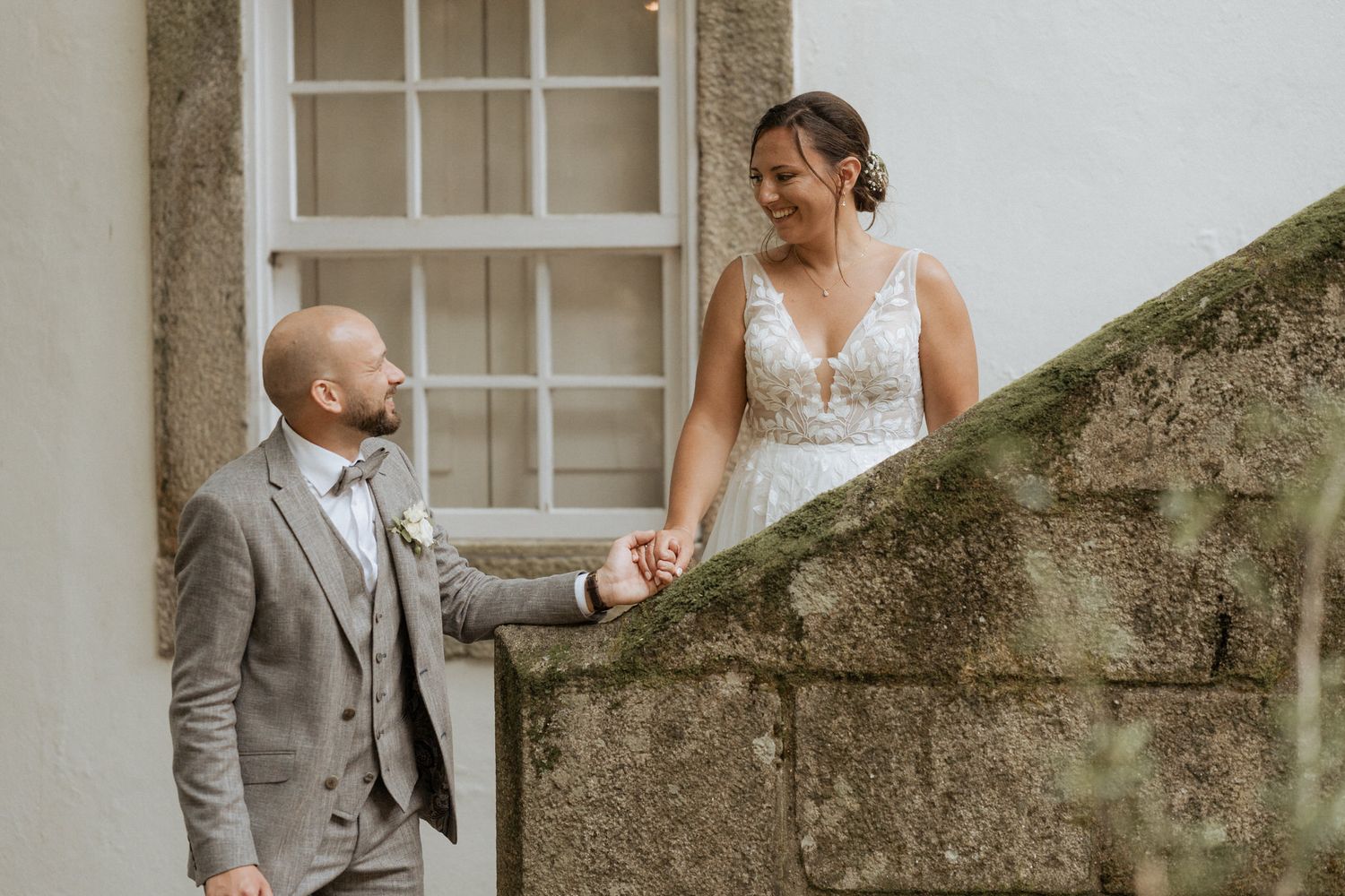 A couple in wedding attire share a romantic moment on stone steps next to a historic white building.