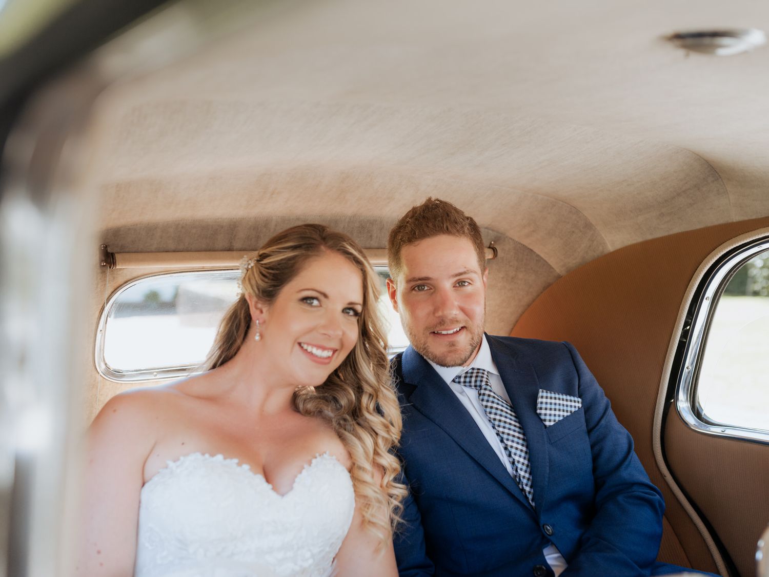 Newlywed couple sitting in the back of a vintage car with elegant interior on their wedding day.