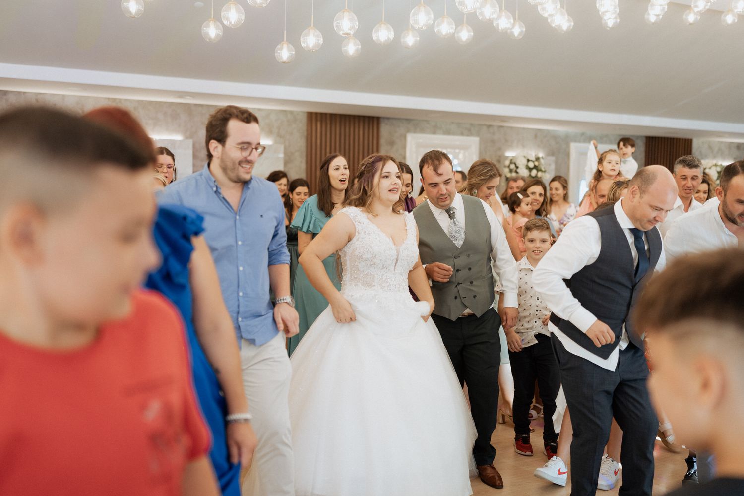 Wedding guests dance and celebrate on a brightly lit dance floor during a joyous reception.