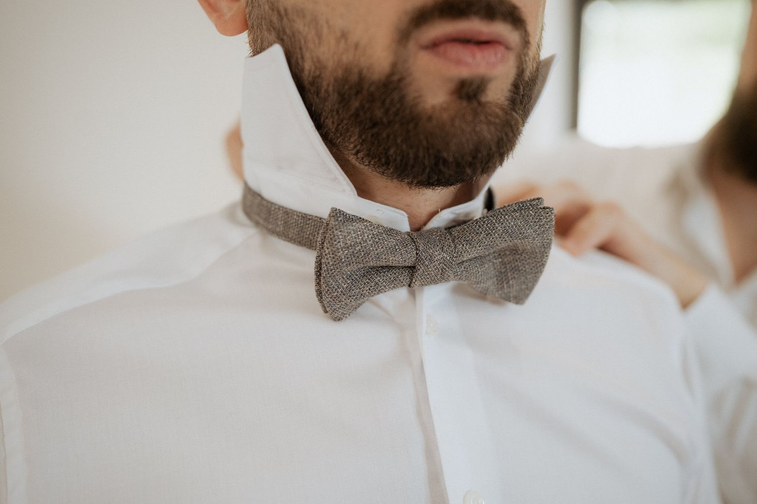 Close-up of a gray tweed bow tie worn with crisp white shirt collar and partial beard visible.