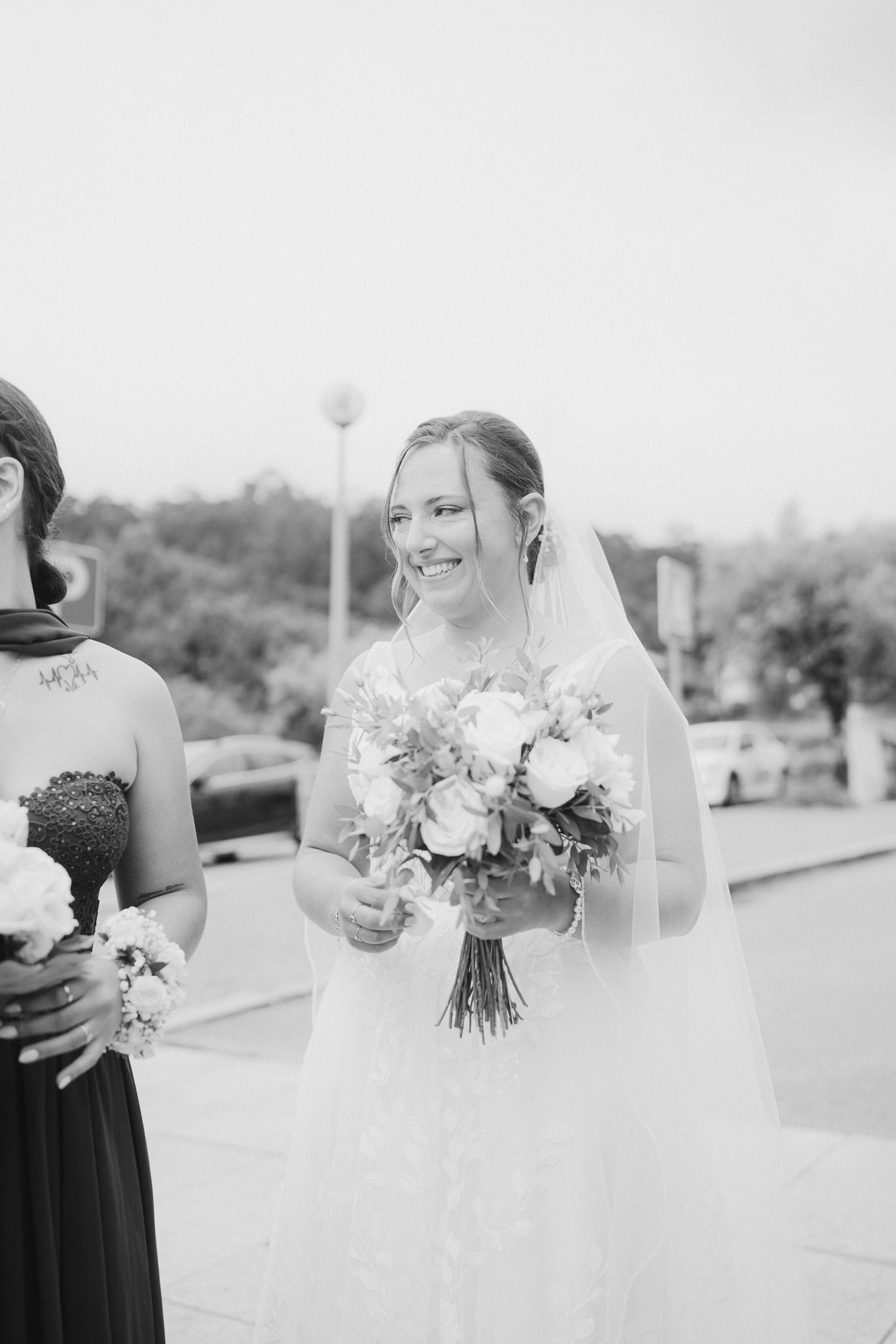 Black and white wedding photo showing a bride holding a delicate bouquet of flowers and wearing a flowing veil.