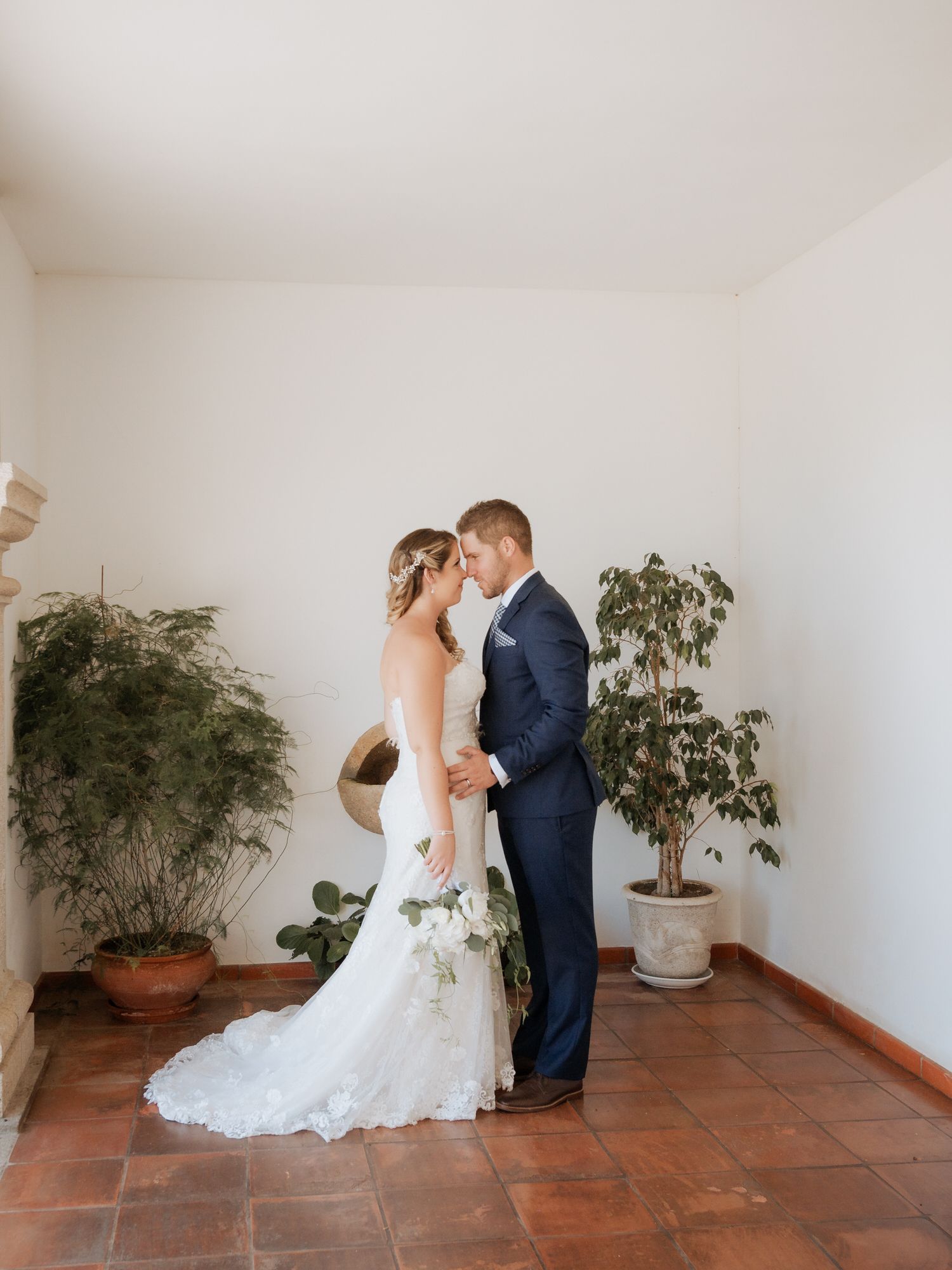 A couple shares an intimate moment in a minimalist indoor setting with terracotta floors and potted plants.