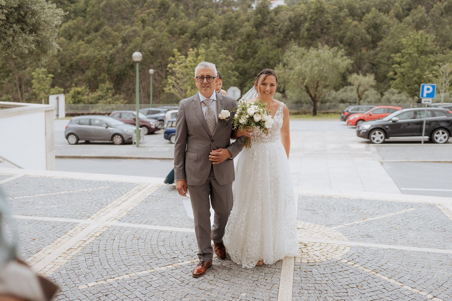 A wedding couple walks arm in arm through a stone paved parking area on their special day.